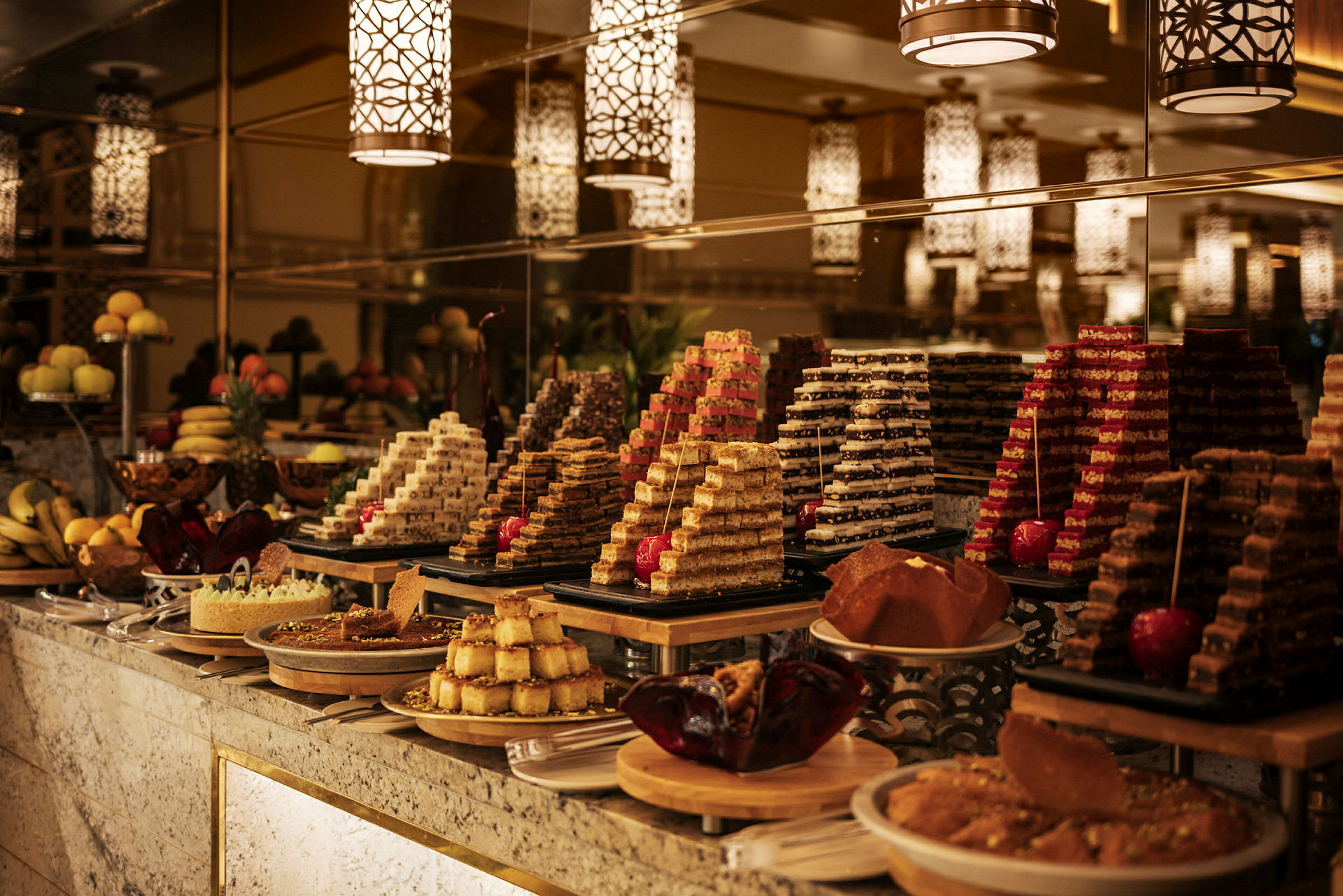 En buffet med forskellige slags kager og desserter præsenteret i pyramider og fade under dekorative lamper. (AI-genereret tekst)
