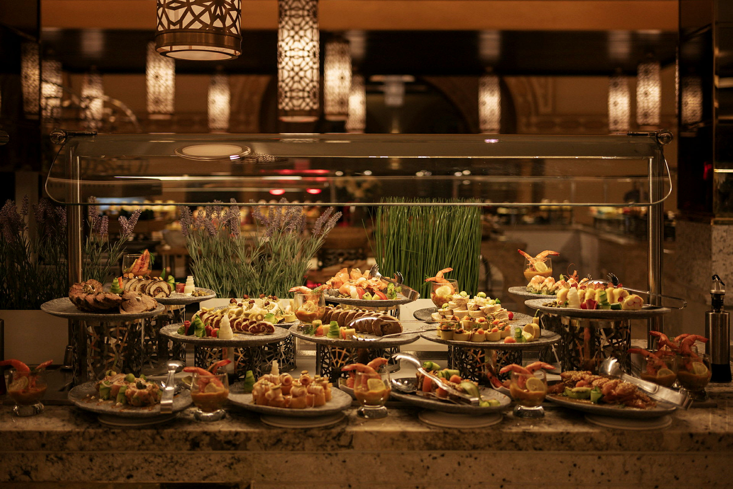 En buffet med forskellige retter præsenteret på metalfade, dekoreret med urter og græs. (AI-genereret tekst)