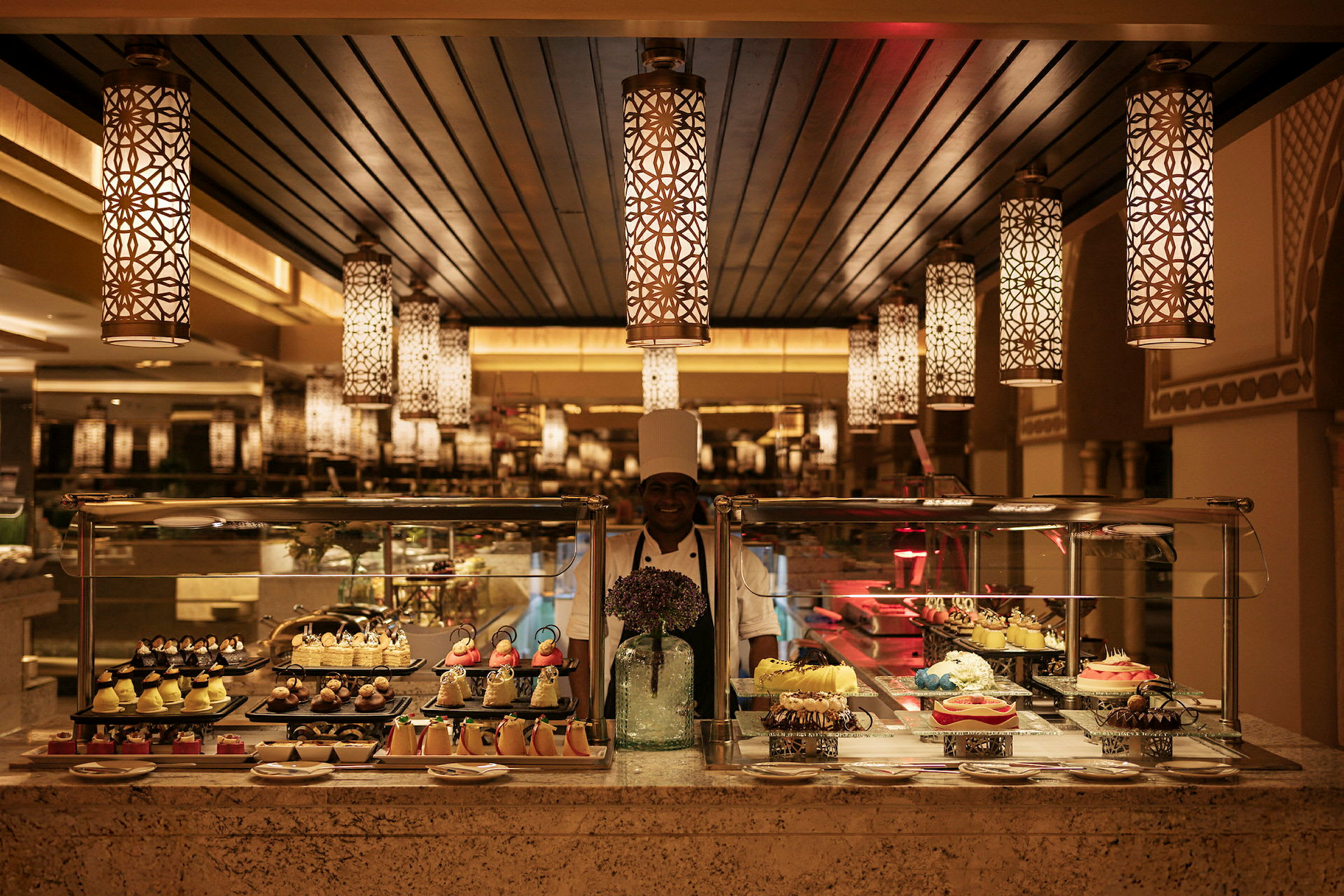Billede af en buffet med forskellige desserter vist på række under dekorative lysekroner. (AI-genereret tekst)
