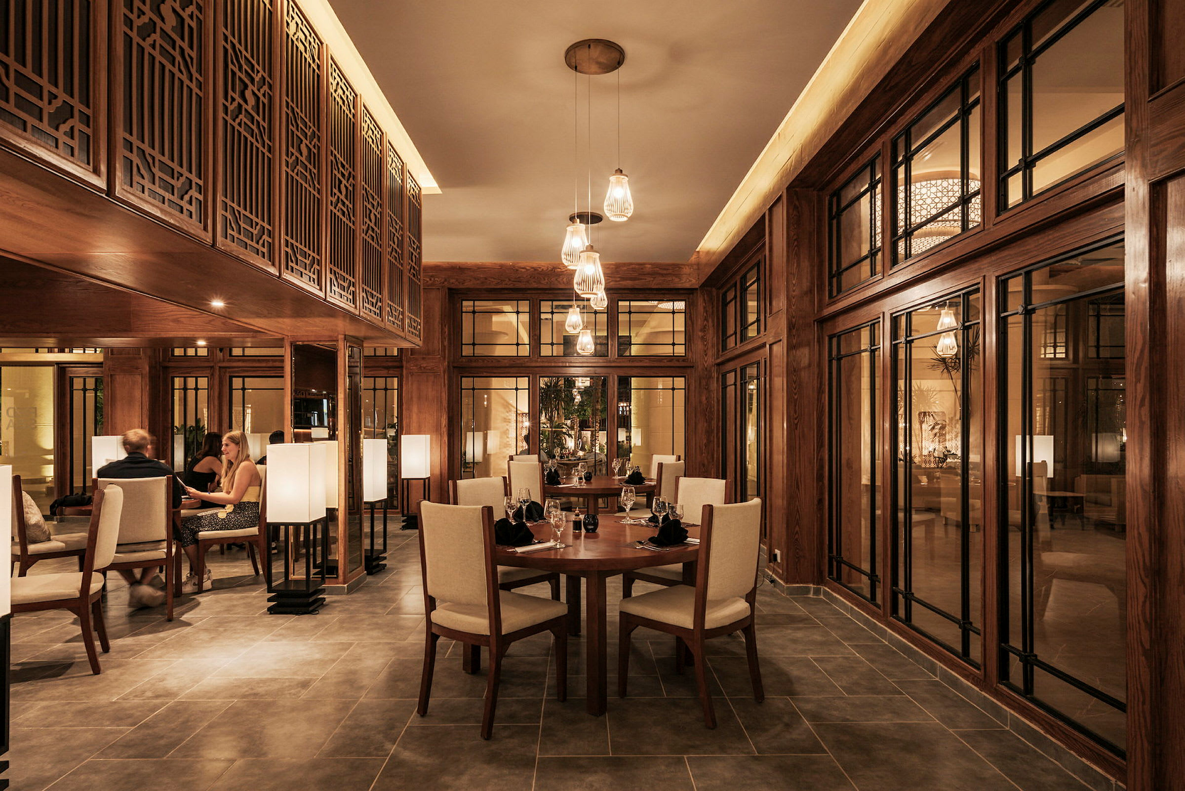 Interiør af en elegant restaurant med træpaneler, runde borde og stole samt dæmpet belysning. (AI-genereret tekst)