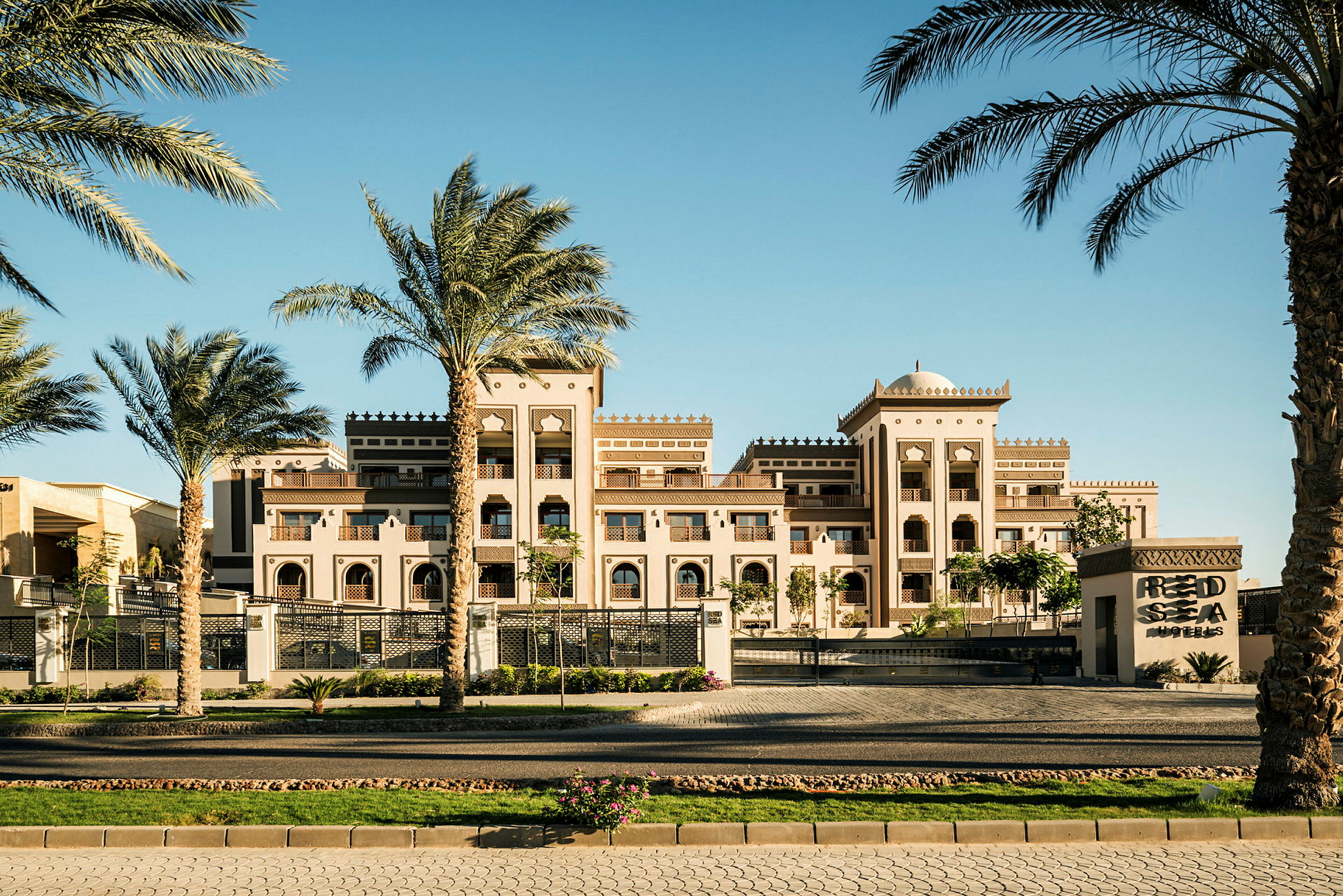 Et elegant hotelkompleks i arabisk stil med palmer i forgrunden under en klar blå himmel. (AI-genereret tekst)