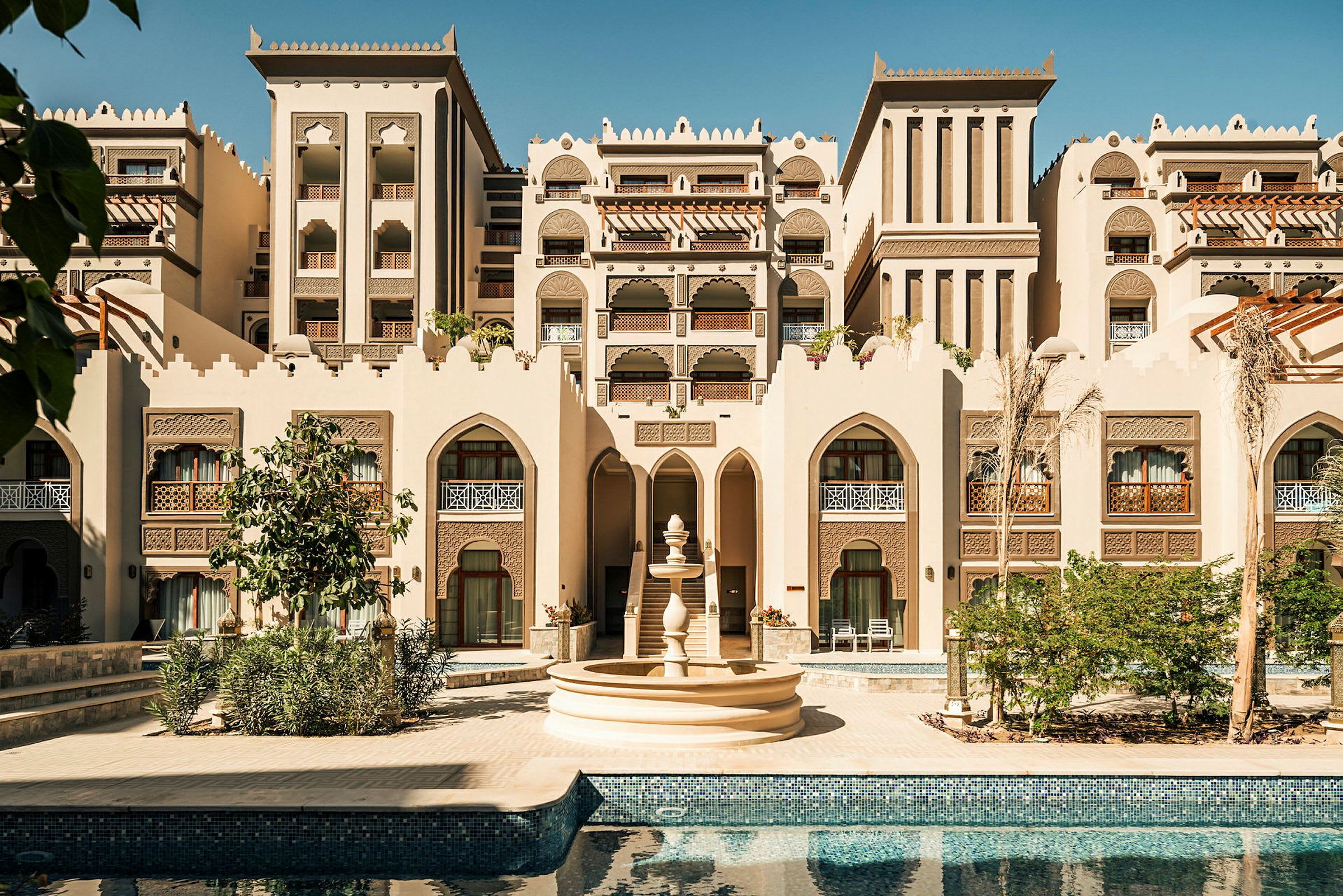 En bygning i arabisk arkitekturstil med en fontæne og en pool i forgrunden. (AI-genereret tekst)