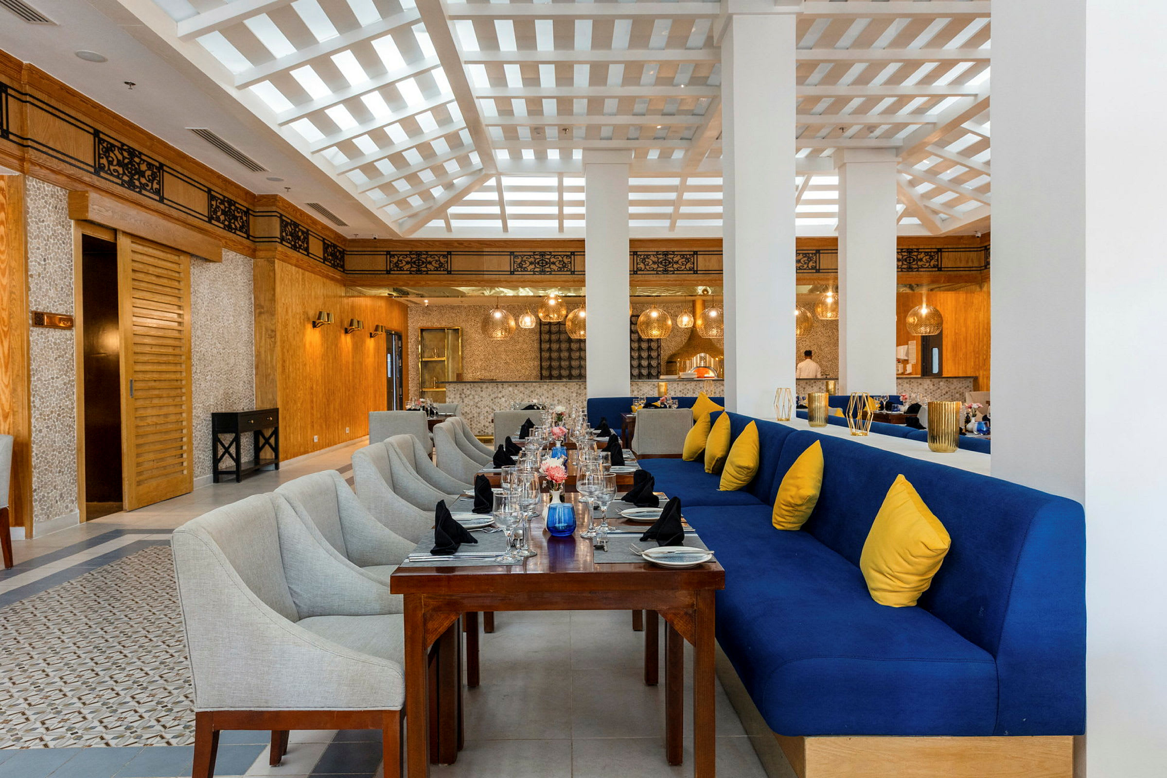 Restaurant med dækkede borde og blå sofa med gule puder. (AI-genereret tekst)