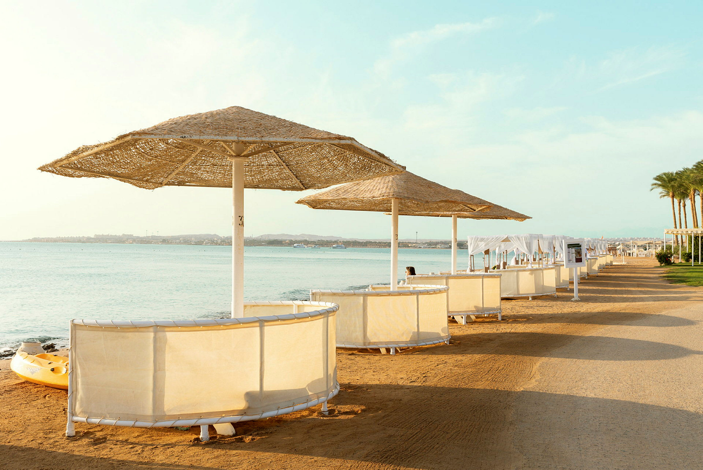 Strand med parasoller og solbåse ved vandet. (AI-genereret tekst)