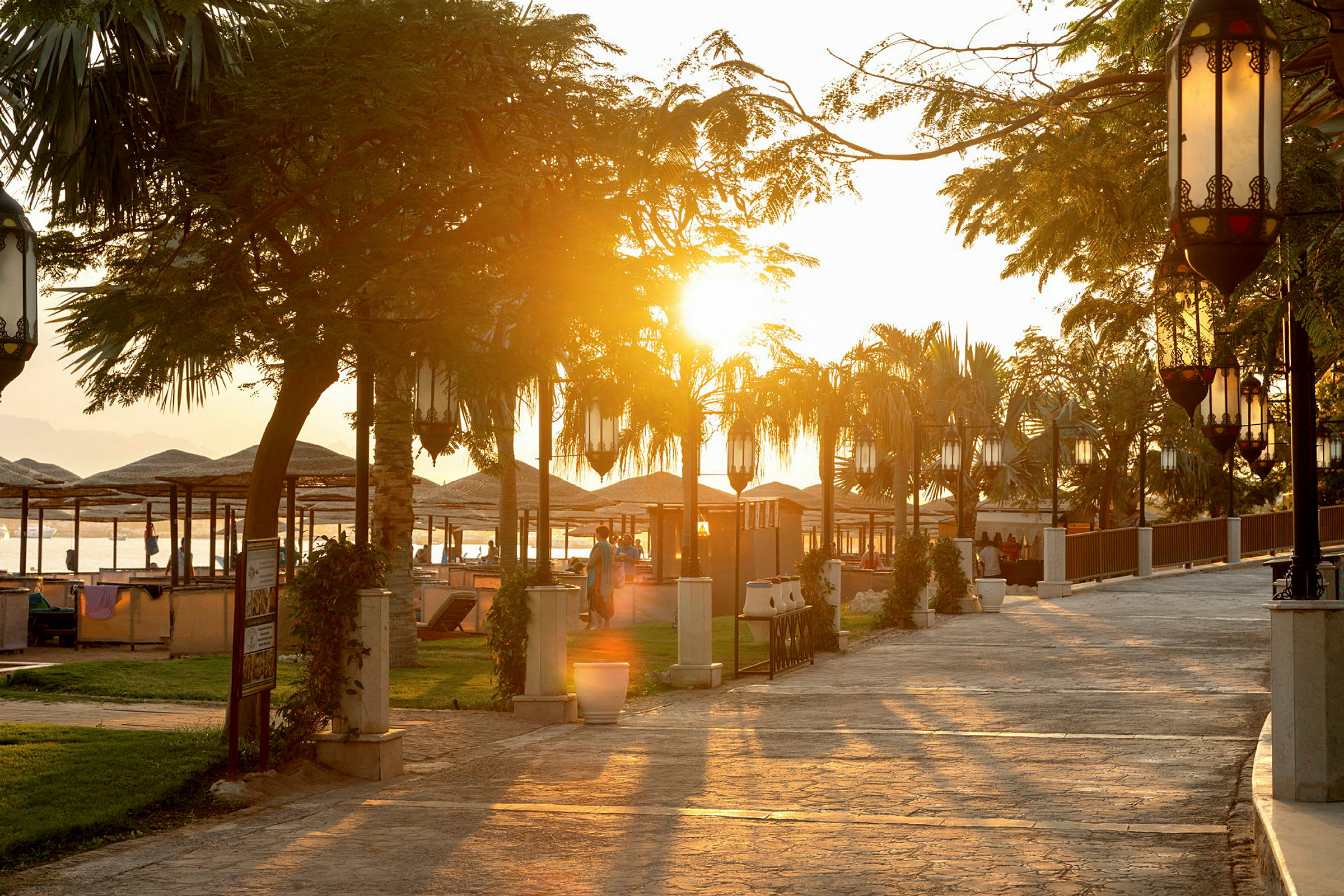 Solnedgang ved en strandpromenade med parasoller og borde. (AI-genereret tekst)