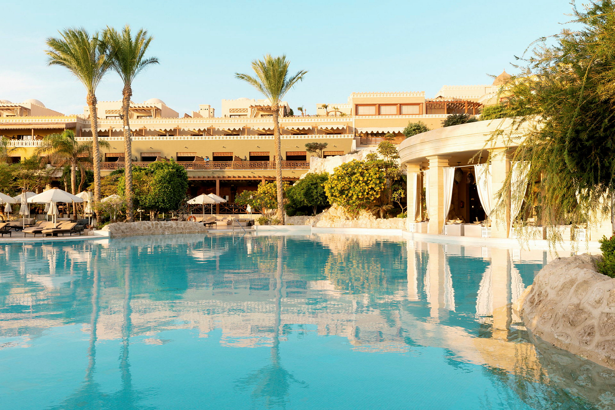 Hotelområde med pool, parasoller og bygninger i baggrunden. (AI-genereret tekst)