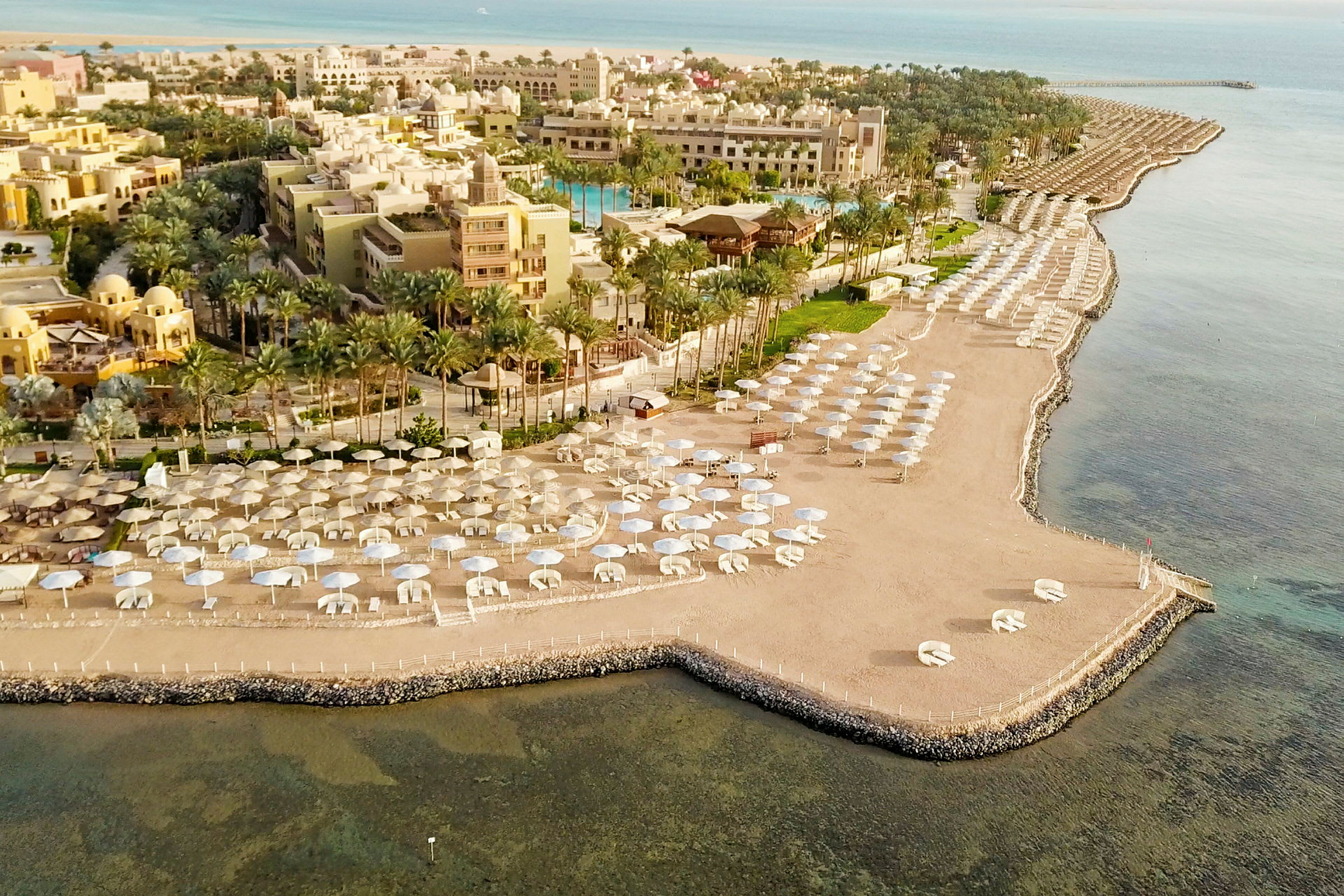 Luftfoto af en strand med parasoller og hotelbygninger i baggrunden. (AI-genereret tekst)