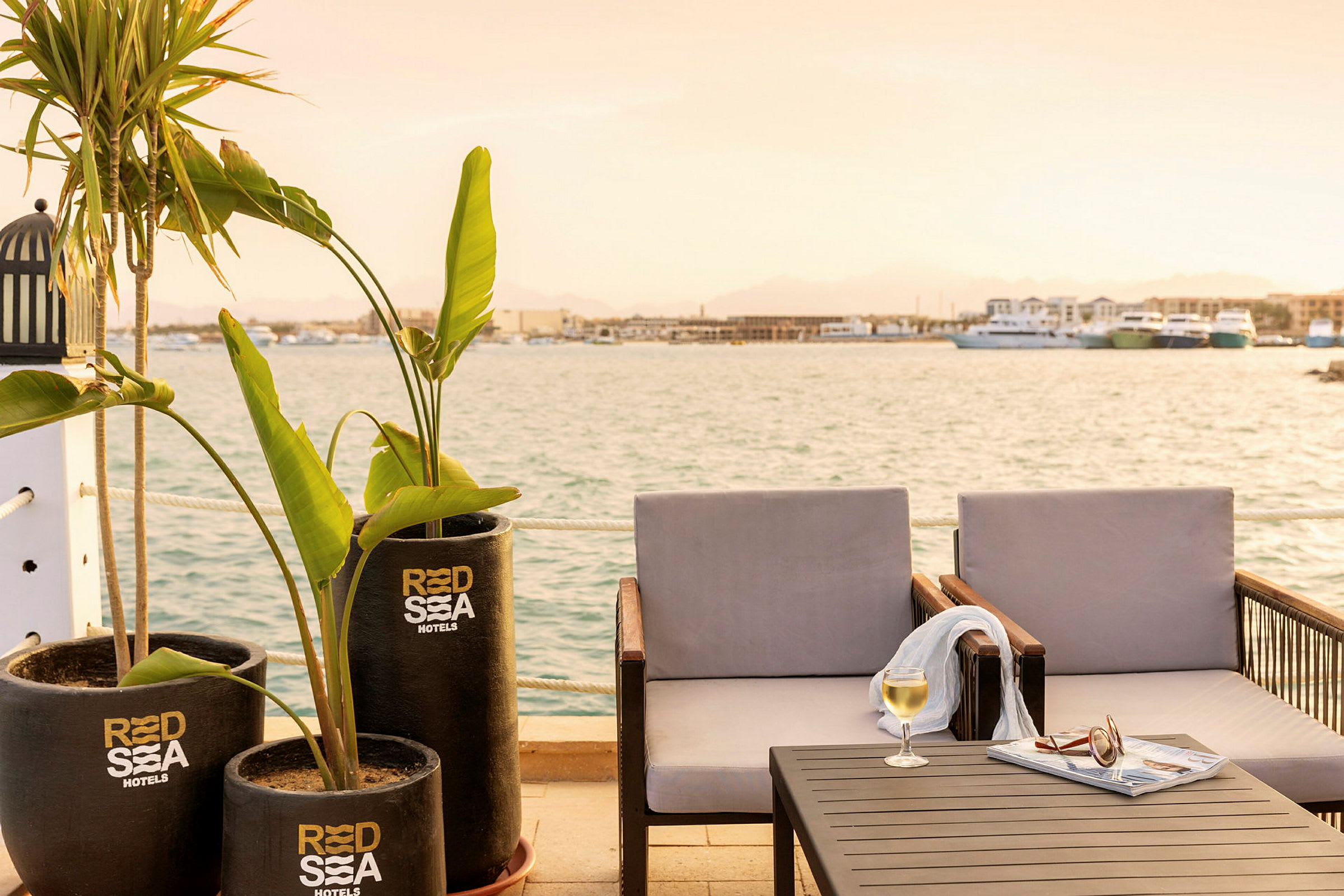 Udendørs miljø ved havet med to stole, bord, planter og et glas vin. (AI-genereret tekst)