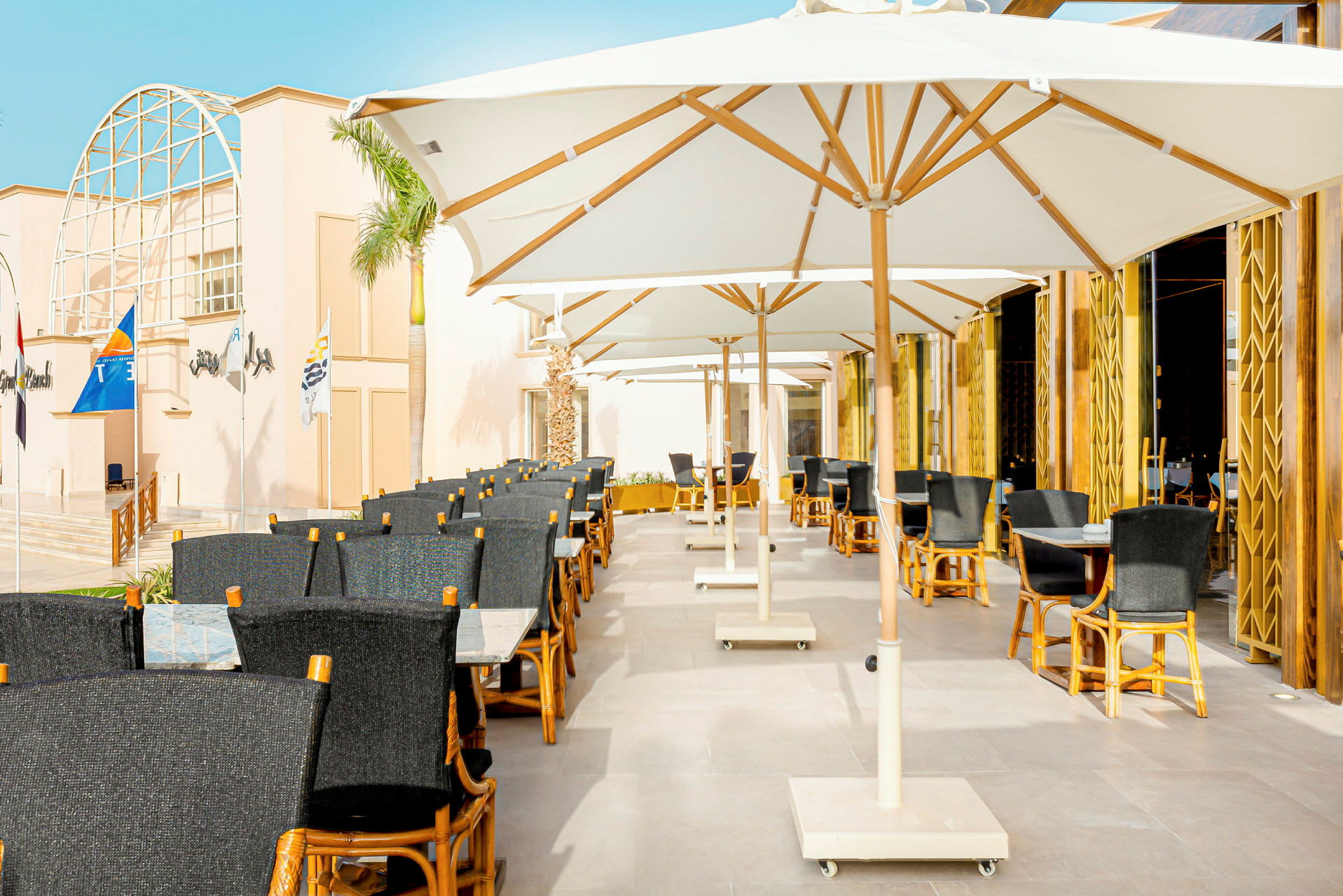 Udendørs restaurant med hvide parasoller og stole af træ og mørkt stof. (AI-genereret tekst)