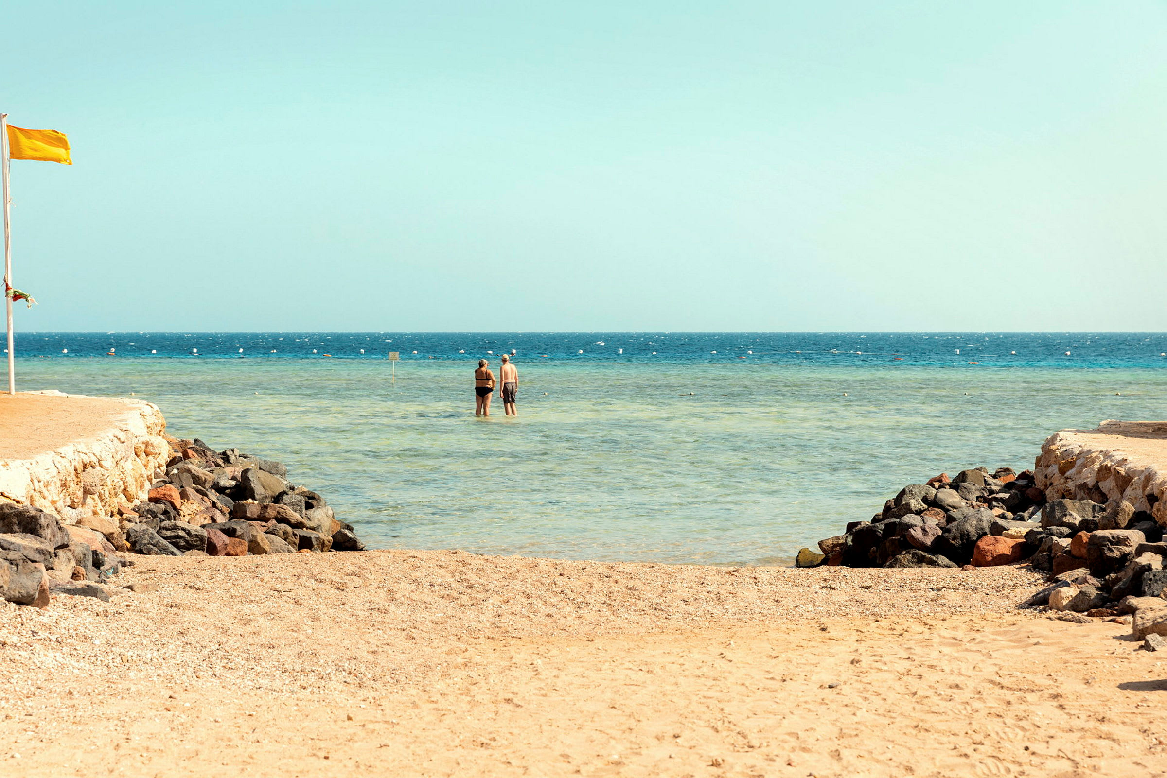 To personer står i lavt vand ved en strand. (AI-genereret tekst)