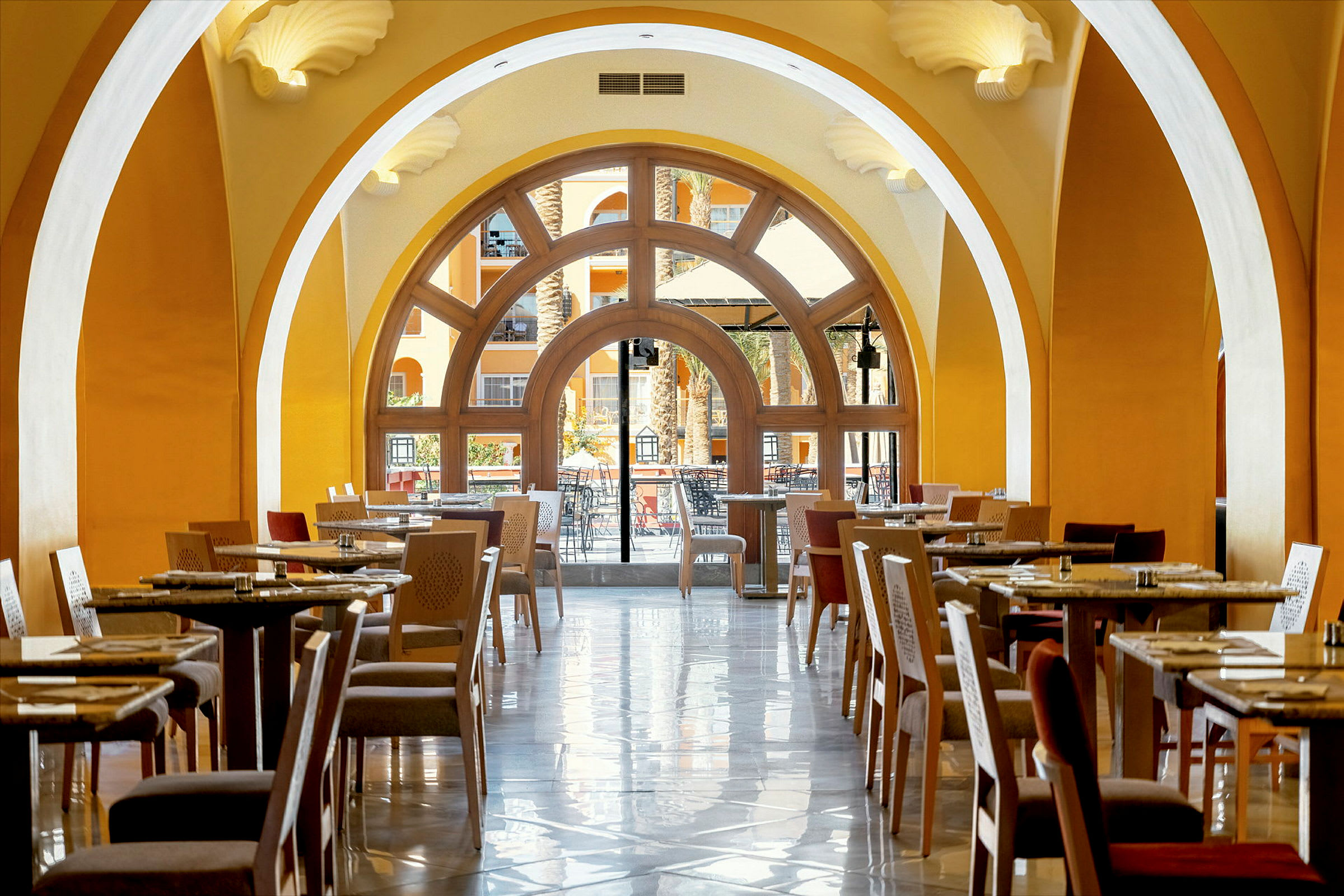 En restaurant med siddepladser og borde under hvælvede lofter med udsigt til en terrasse gennem store vinduer. (AI-genereret tekst)