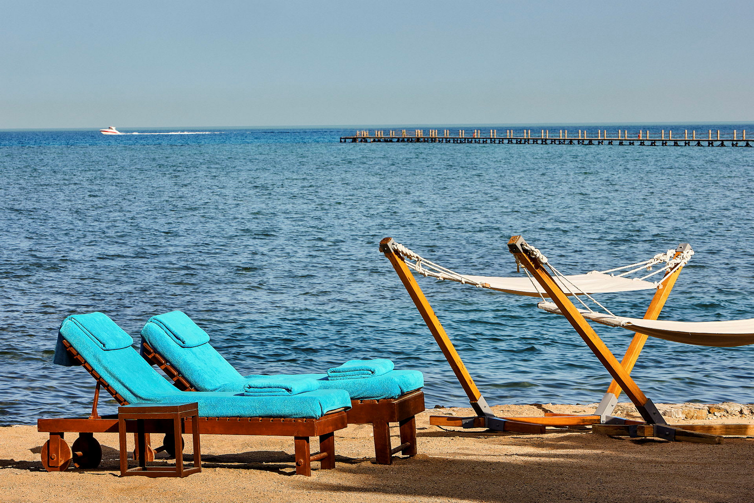 To solsenge med blå hynder og to hængekøjer ved en strand med havudsigt. (AI-genereret tekst)