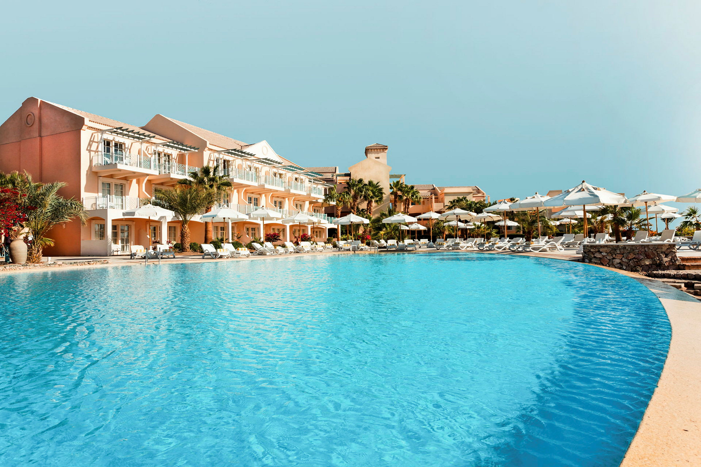 Poolområde ved hotel med parasoller og liggestole. (AI-genereret tekst)