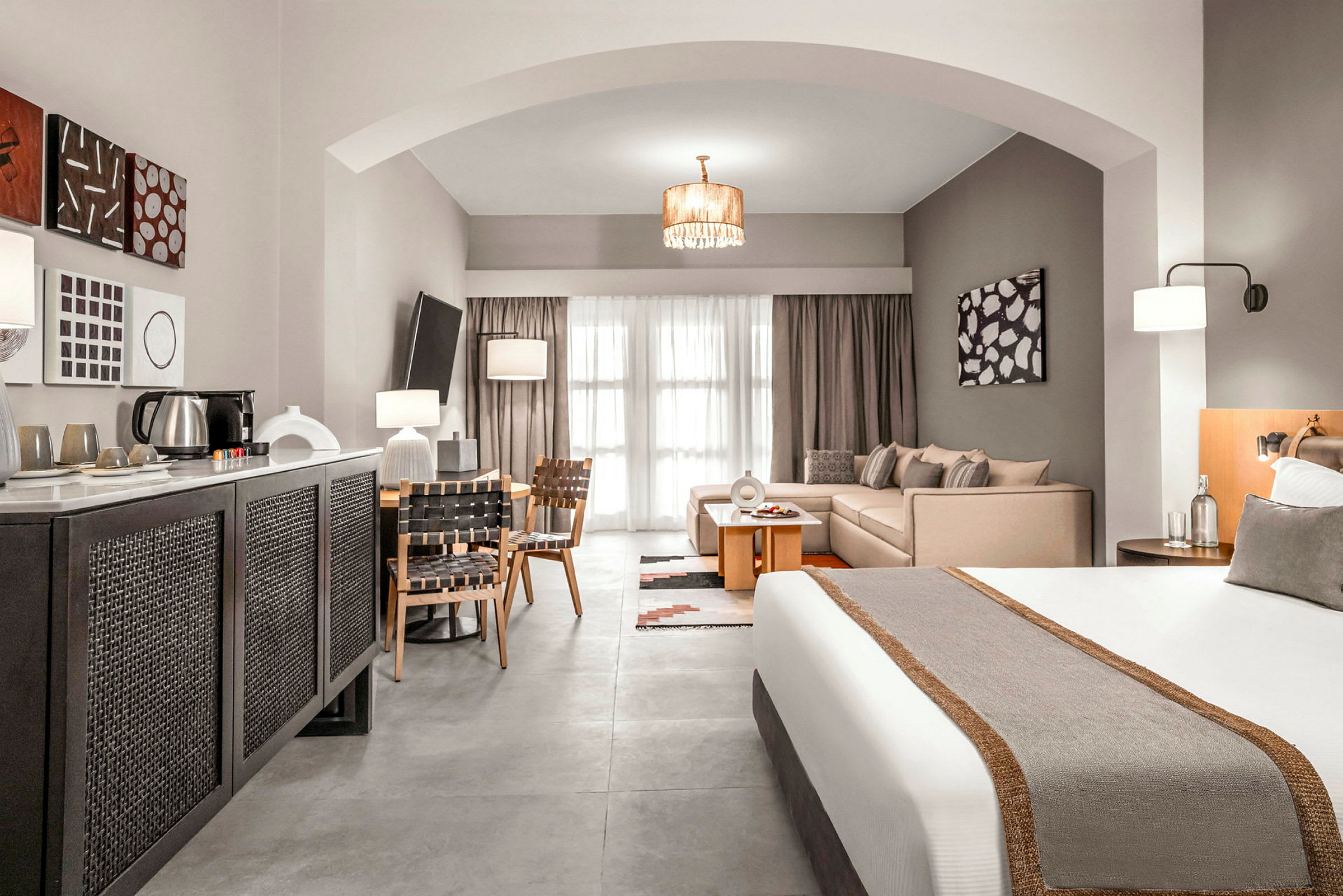 Et hotelværelse med en seng, siddeområde og spisebord samt moderne indretning. (AI-genereret tekst)