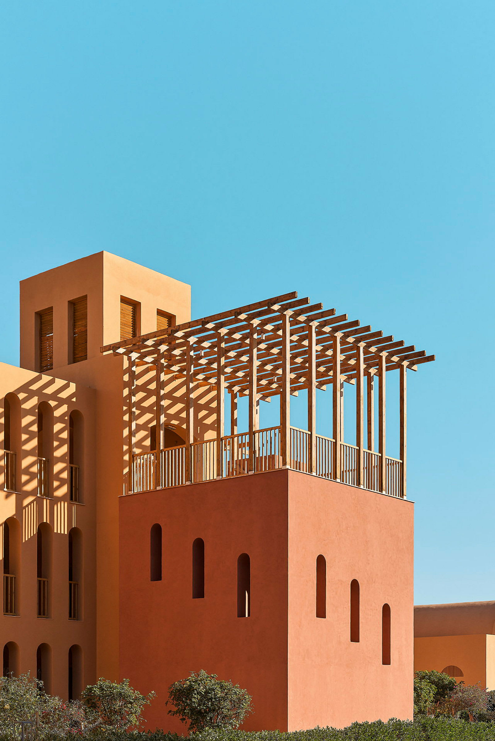 En bygning med træpergola og orange facade mod blå himmel. (AI-genereret tekst)