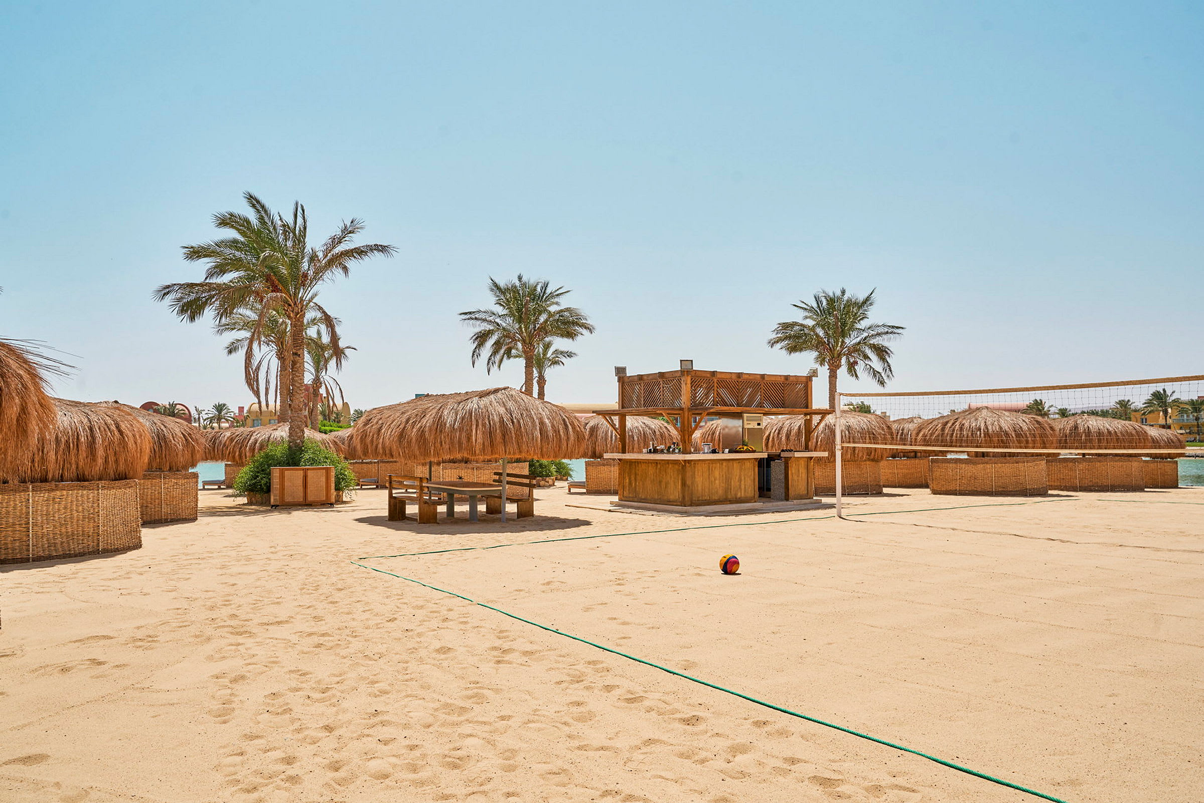 Strand med sand, palmer og parasoller samt en beachvolleybane. (AI-genereret tekst)