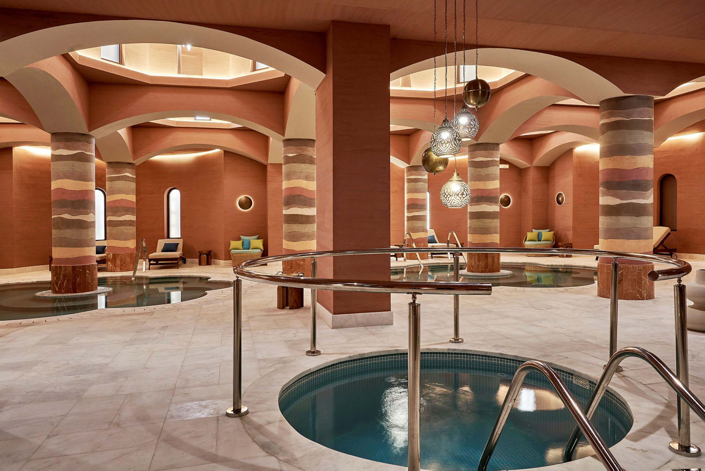 Et indendørs spa med pools, siddepladser og dekorative søjler. (AI-genereret tekst)