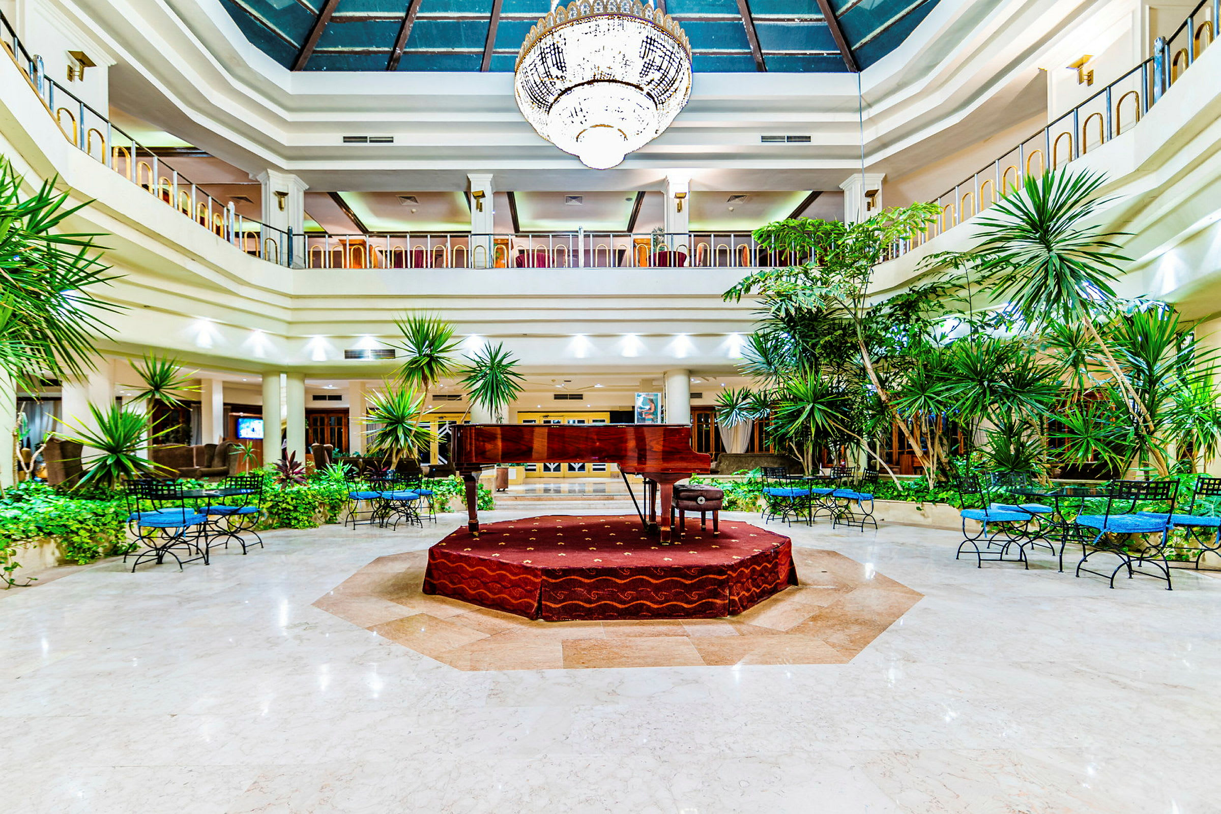 Et flygel placeret på en forhøjet scene i en rummelig hotellobby med planteudsmykninger. (AI-genereret tekst)