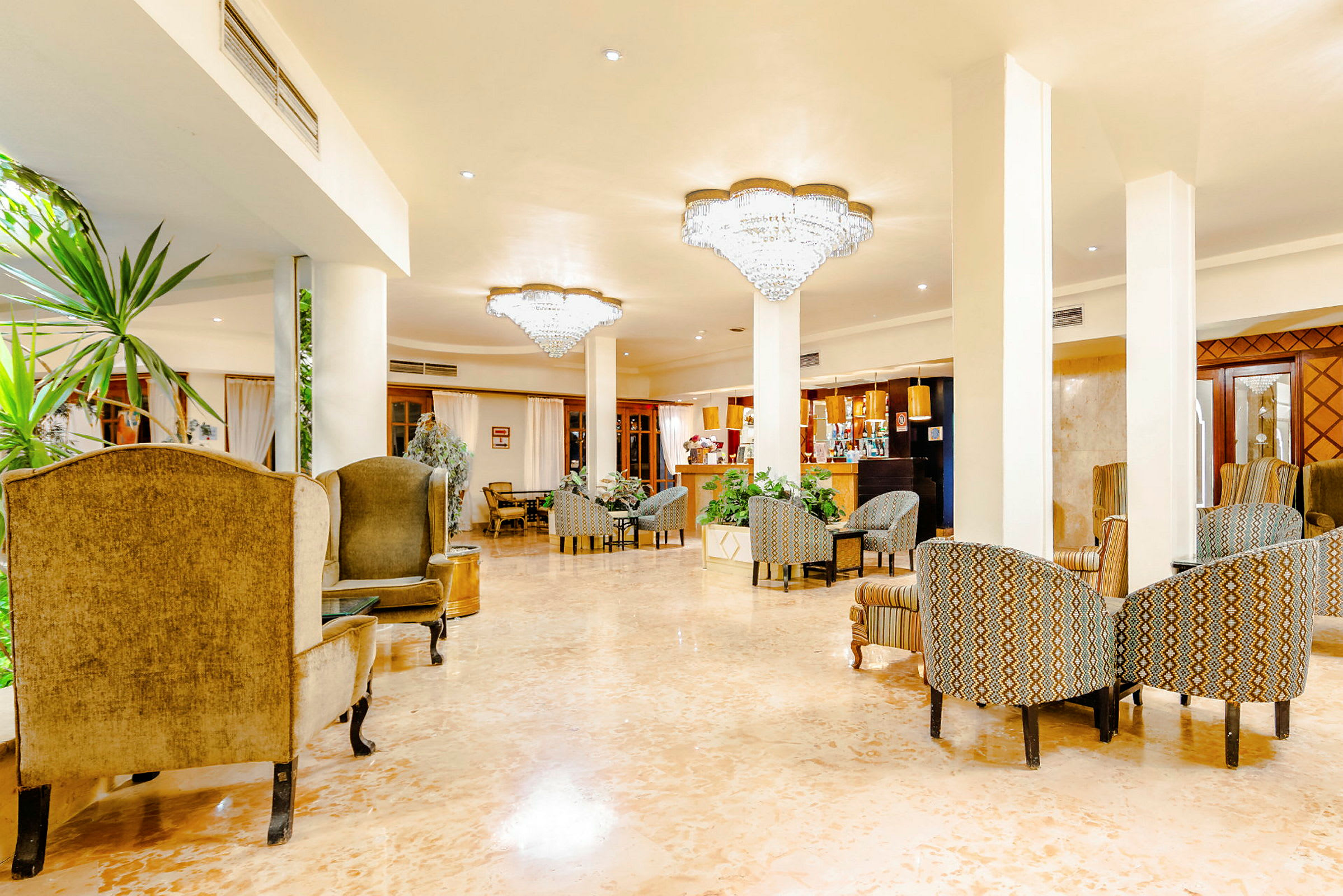 En hotellobby med siddegrupper, grønne planter og lysekroner i loftet. (AI-genereret tekst)