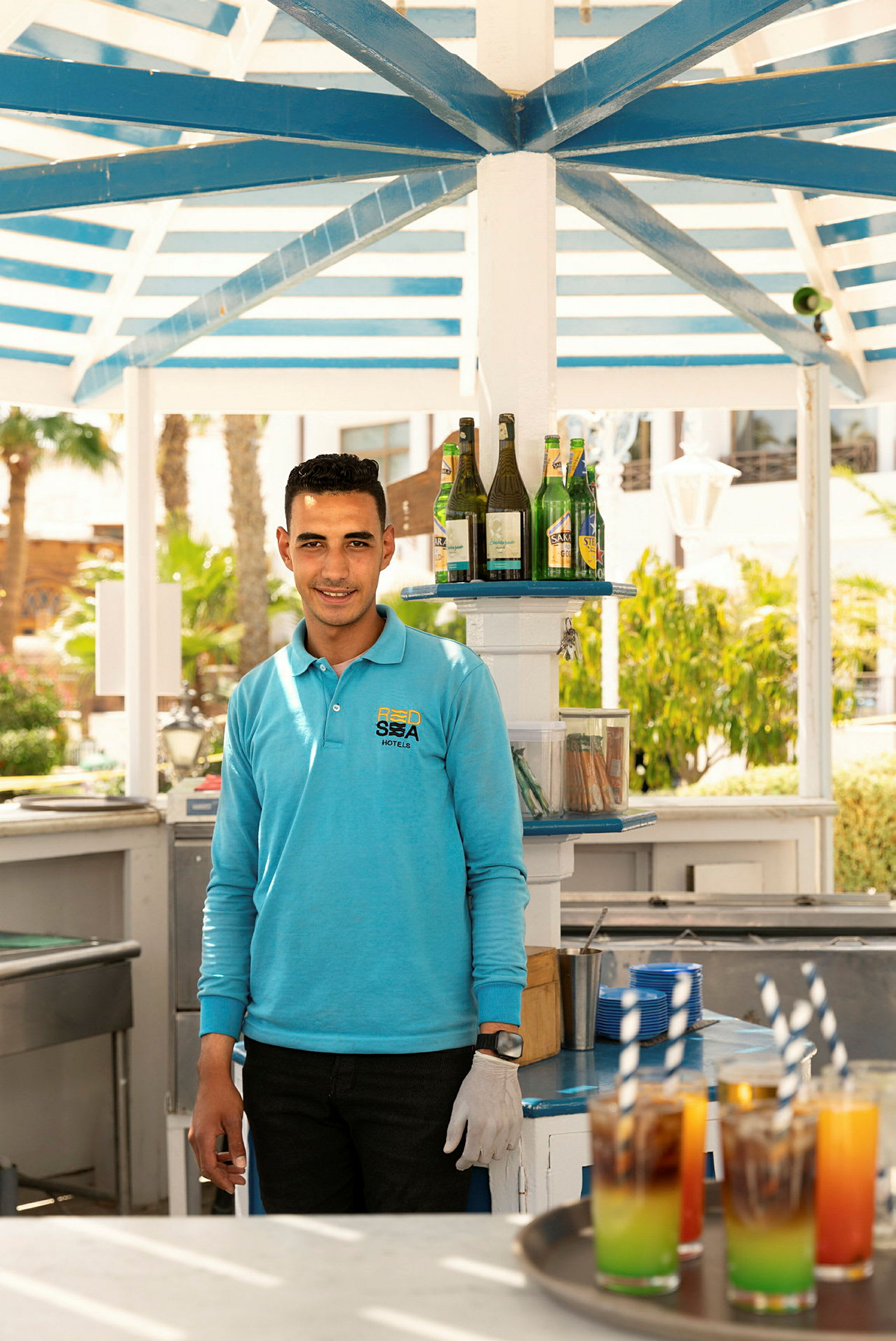 En drinkstation under et overdække, med farverige drikkevarer og flasker på en hylde. (AI-genereret tekst)