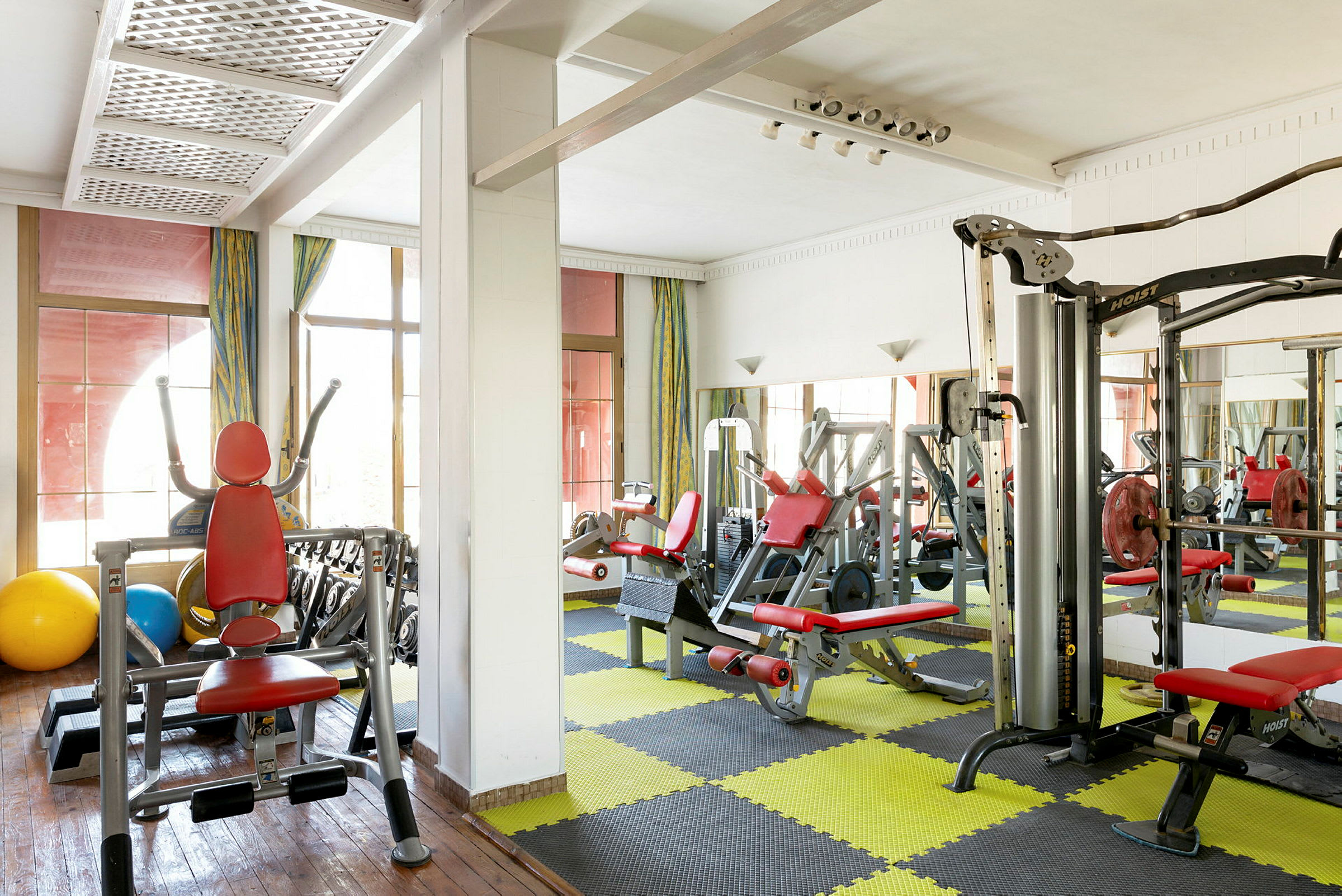 Billede af et fitnesscenter med træningsmaskiner og gul-sort mønstret gulvmåtte. (AI-genereret tekst)