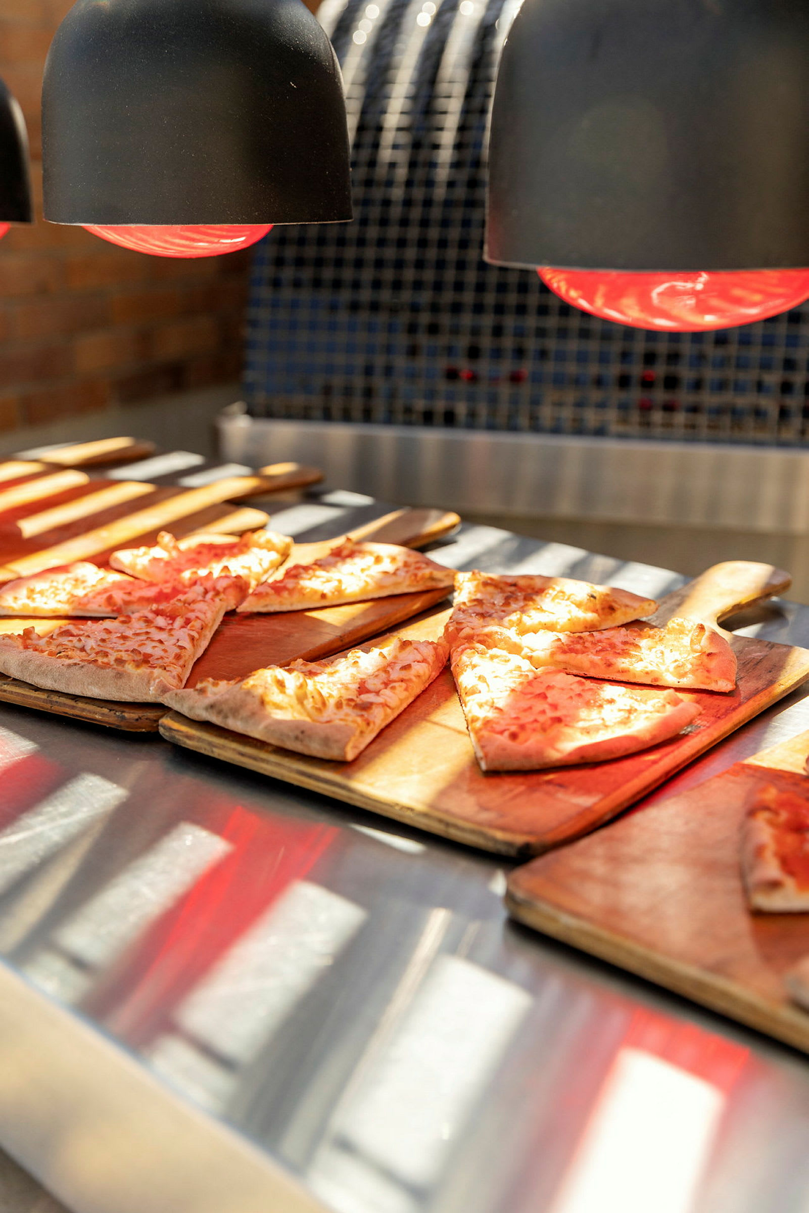 Pizza på skærebrætter under varmelamper. (AI-genereret tekst)