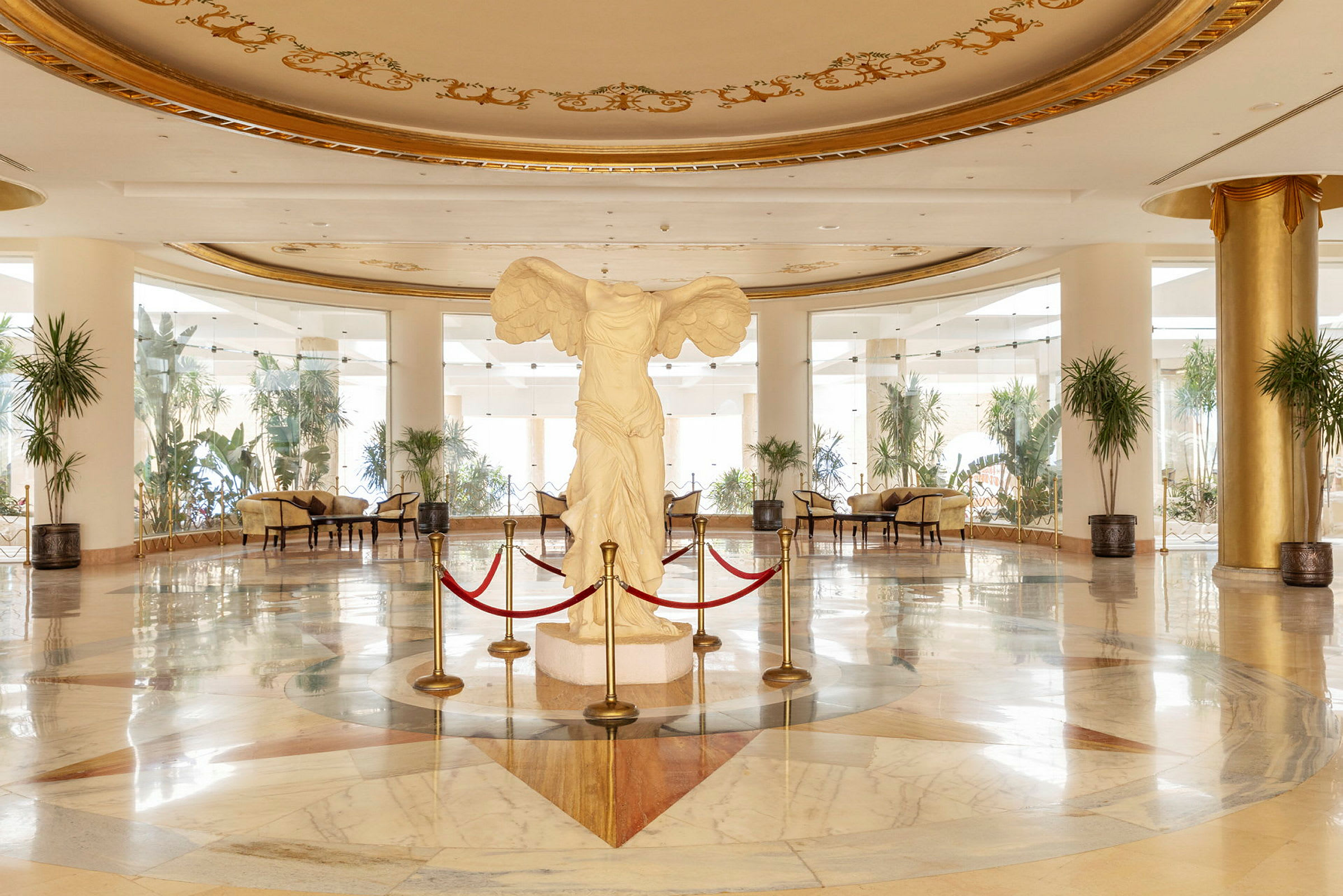 Interiør af en elegant hotellobby med en hvid statue omkranset af røde reb i centrum. (AI-genereret tekst)