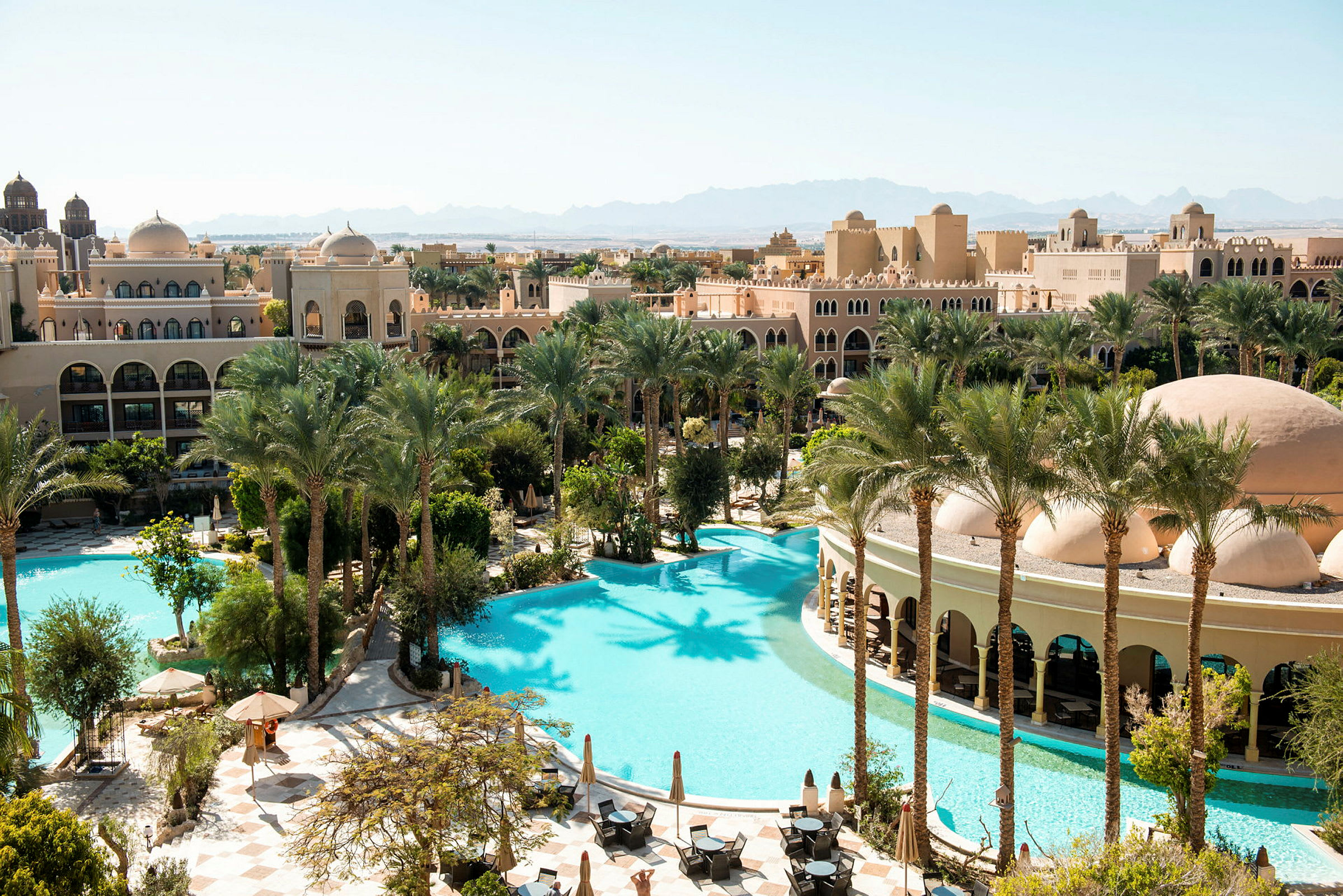 Et hotelområde med pools, palmer og bygninger i arabisk arkitektur. (AI-genereret tekst)
