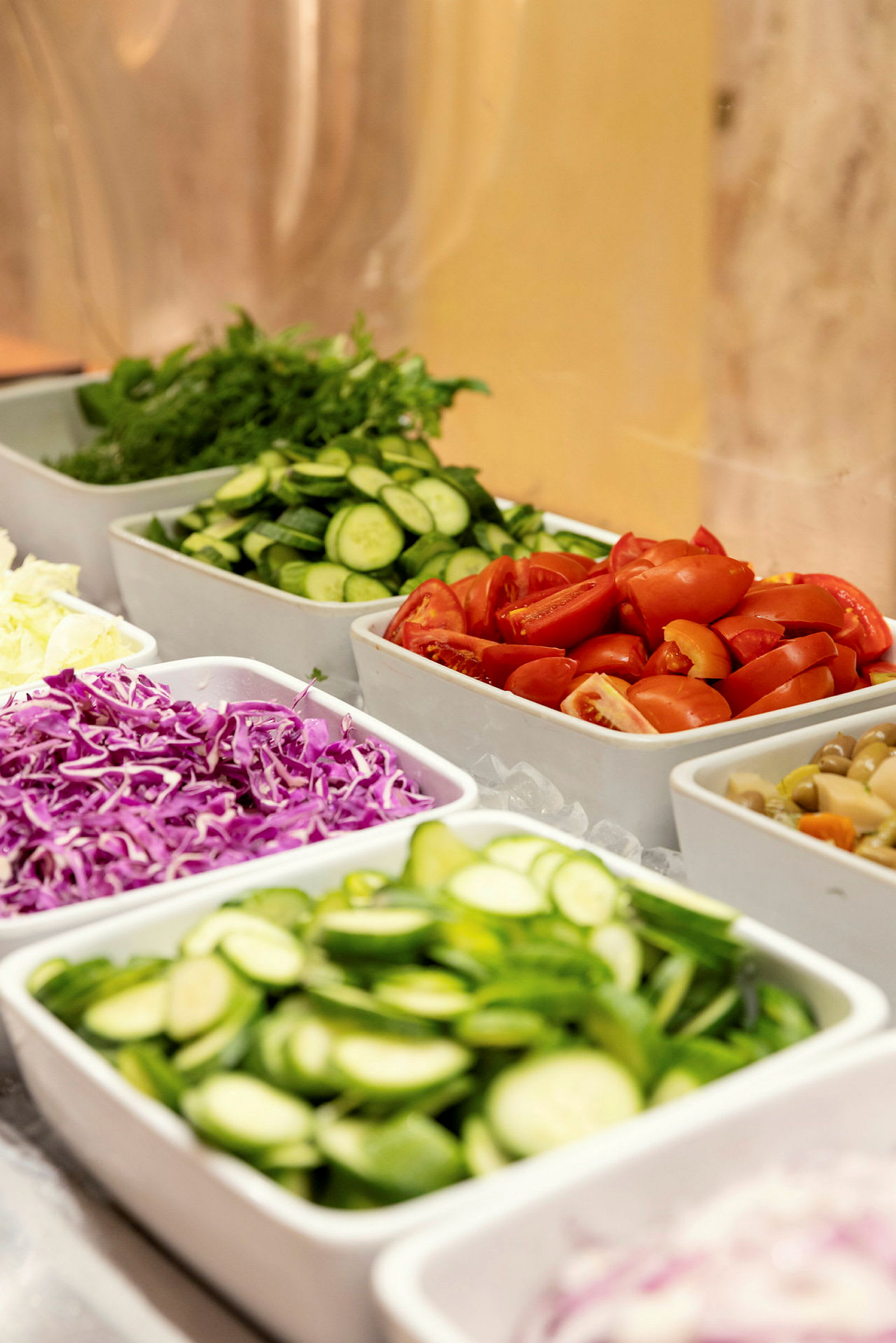 En buffet med forskellige grøntsager som tomater, agurk, rødkål og salat anrettet i hvide skåle. (AI-genereret tekst)