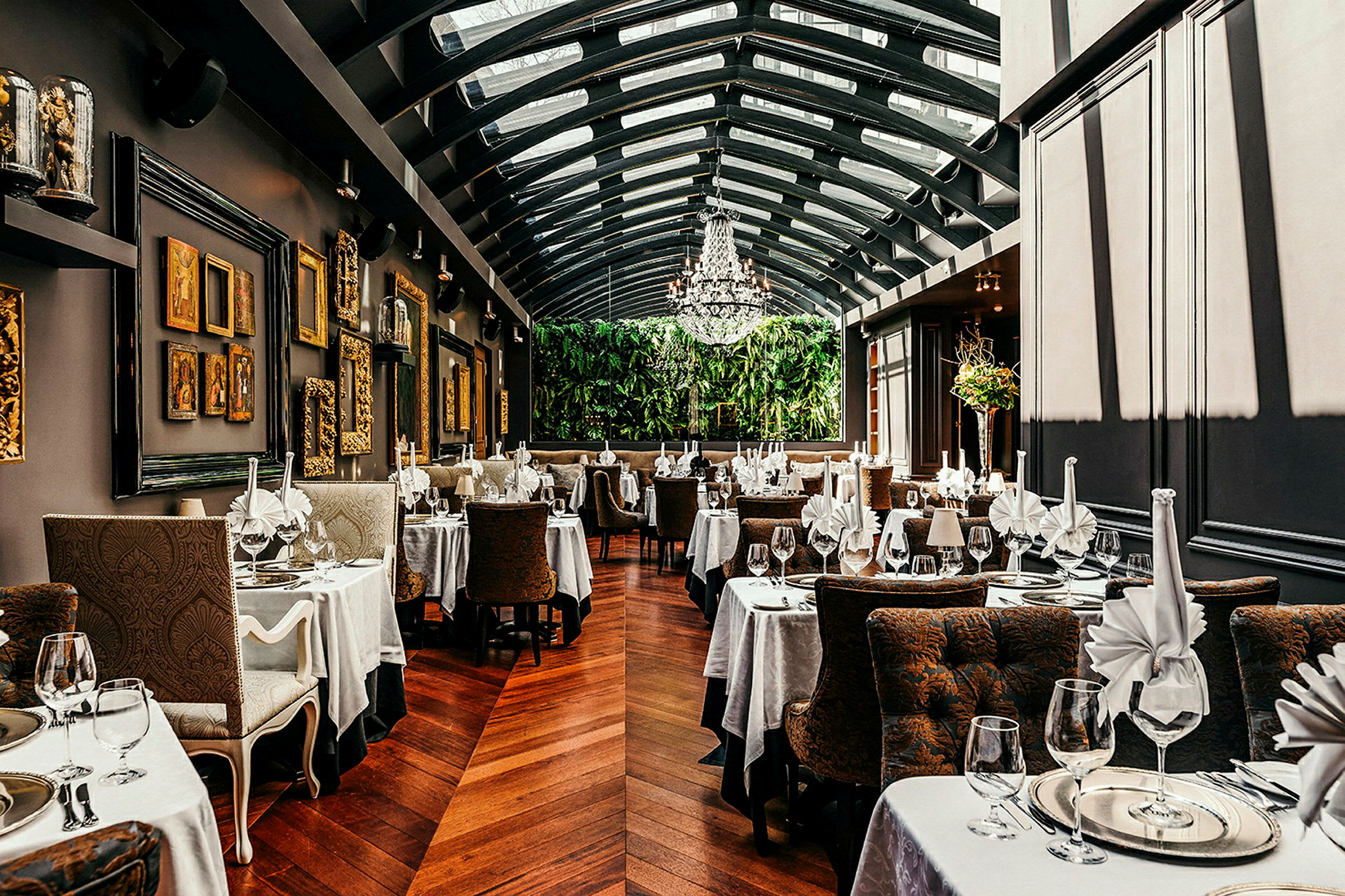 Restaurant med elegante borde, duge og glas. Væggene er dekoreret med kunst, og rummet har glastag. (AI-genereret tekst)