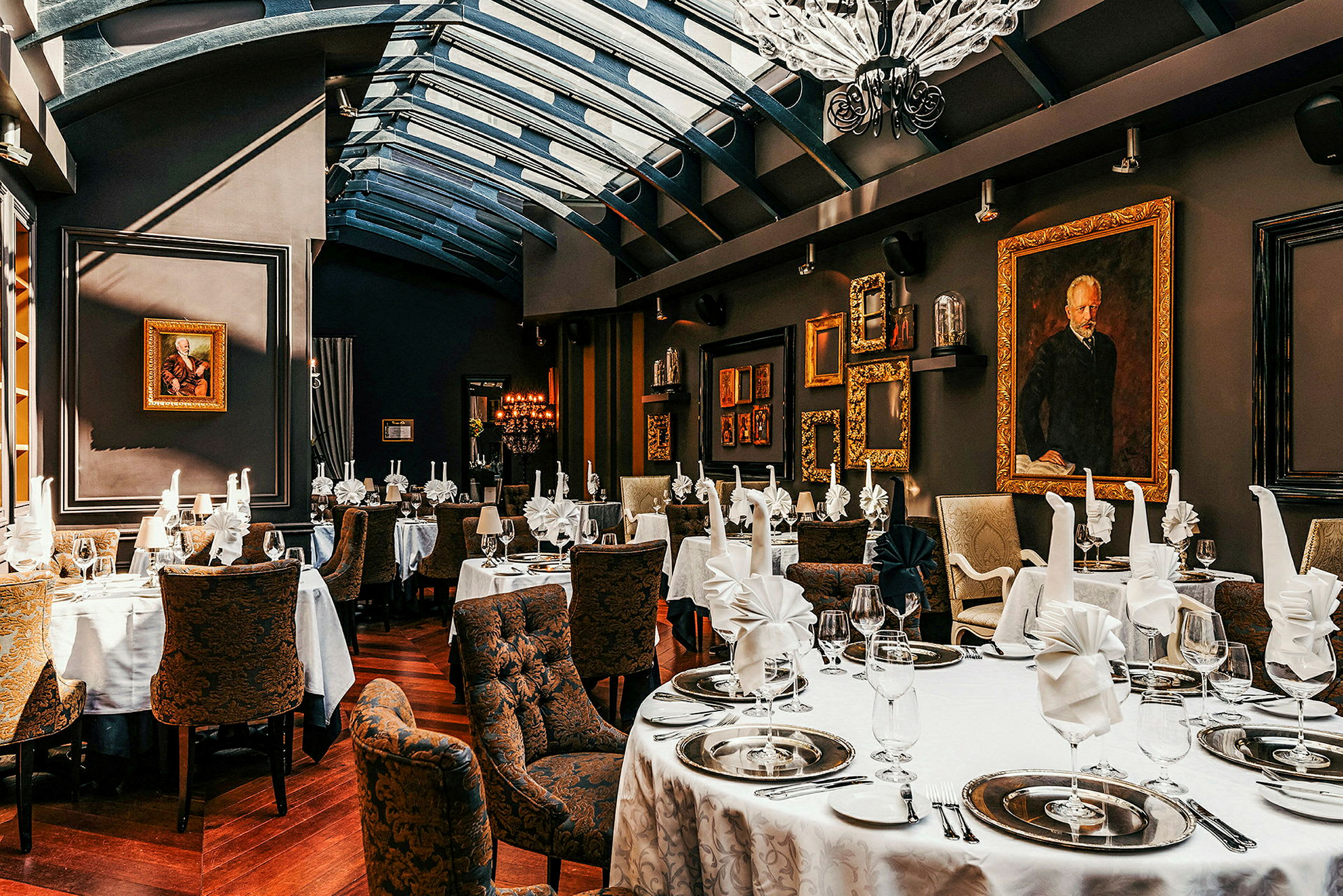 Billedet viser en elegant restaurant med dækkede borde, hvide duge, foldede servietter og dekorative tallerkener. Væggene er dekoreret med kunstværker og guldrammer. (AI-genereret tekst)