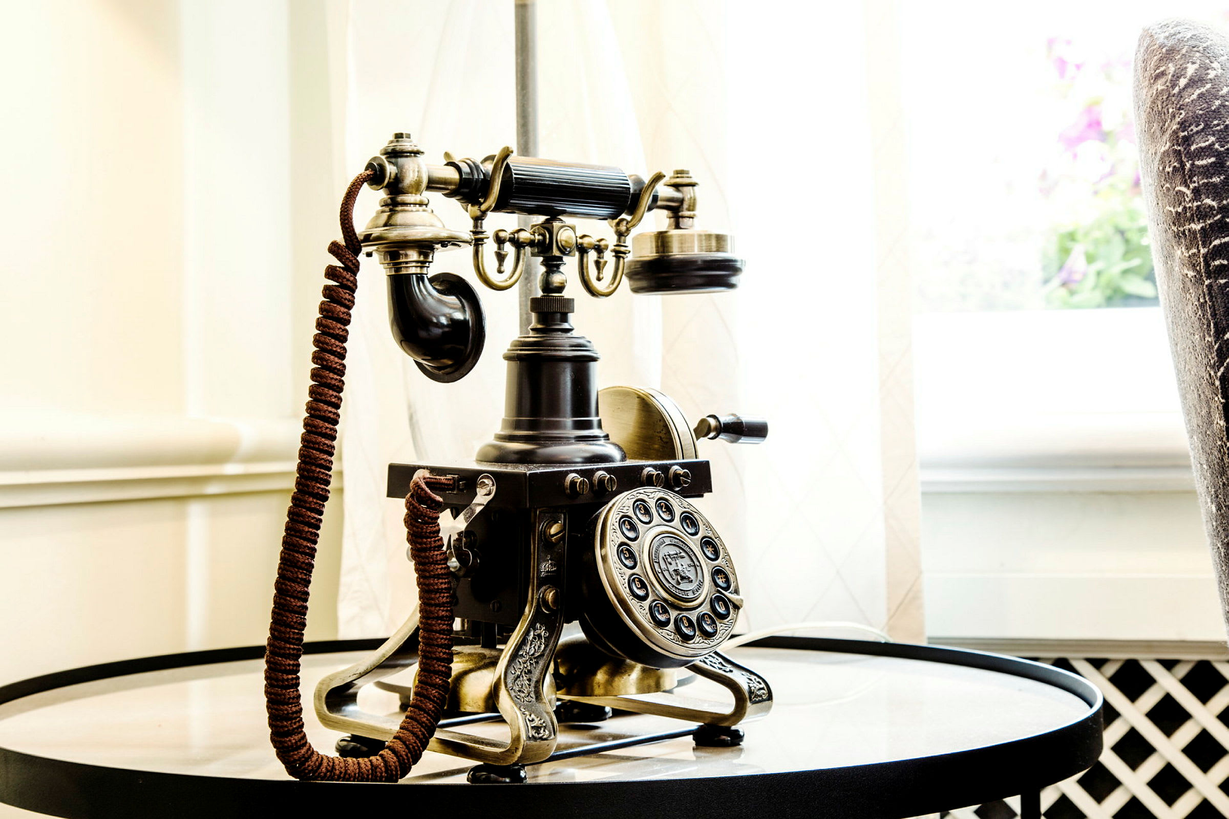 Antik telefon på et rundt bord nær en lyskilde. (AI-genereret tekst)