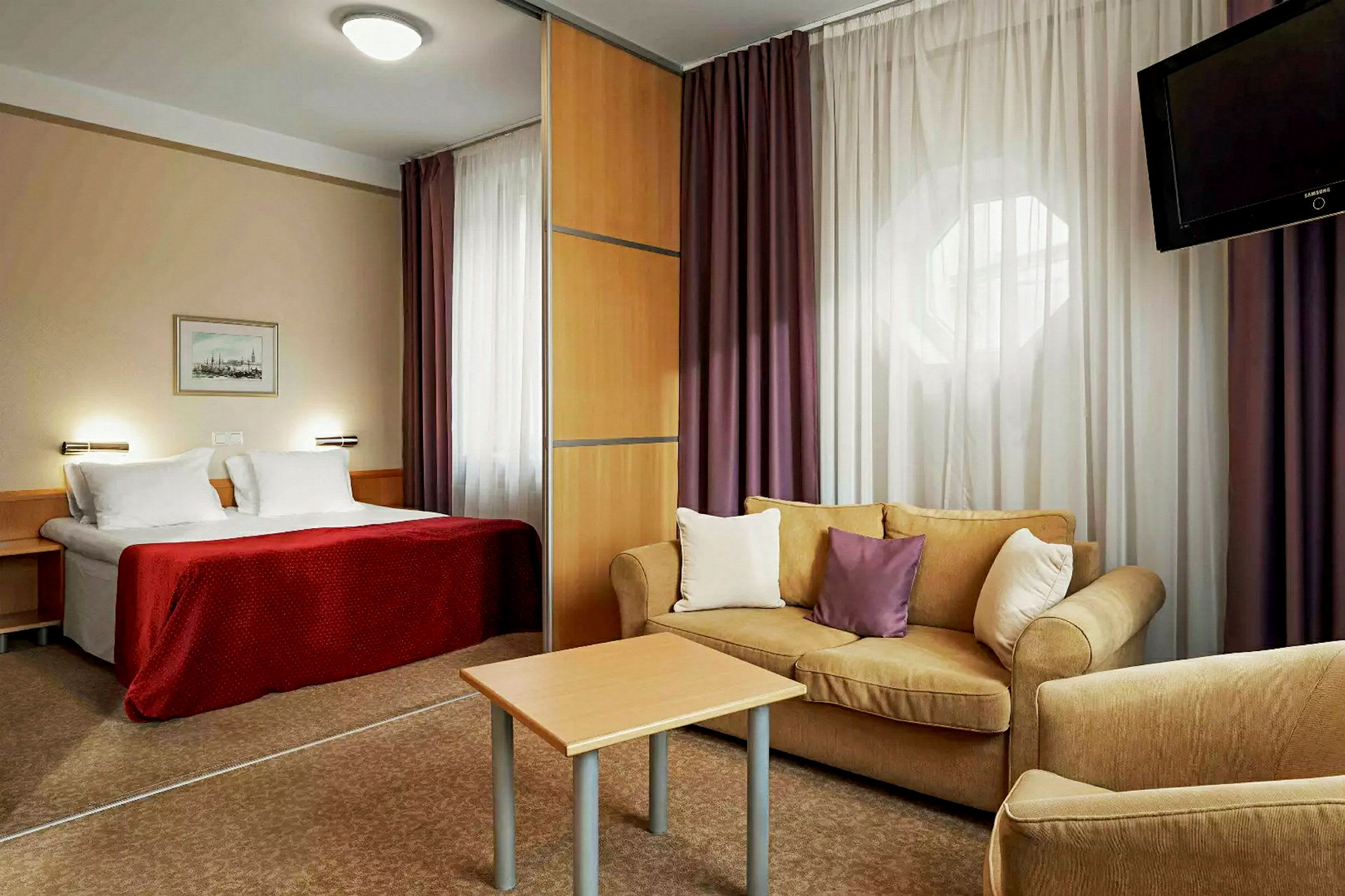 Hotelværelse med en seng, en stue med sofa og et bord samt en TV. (AI-genereret tekst)