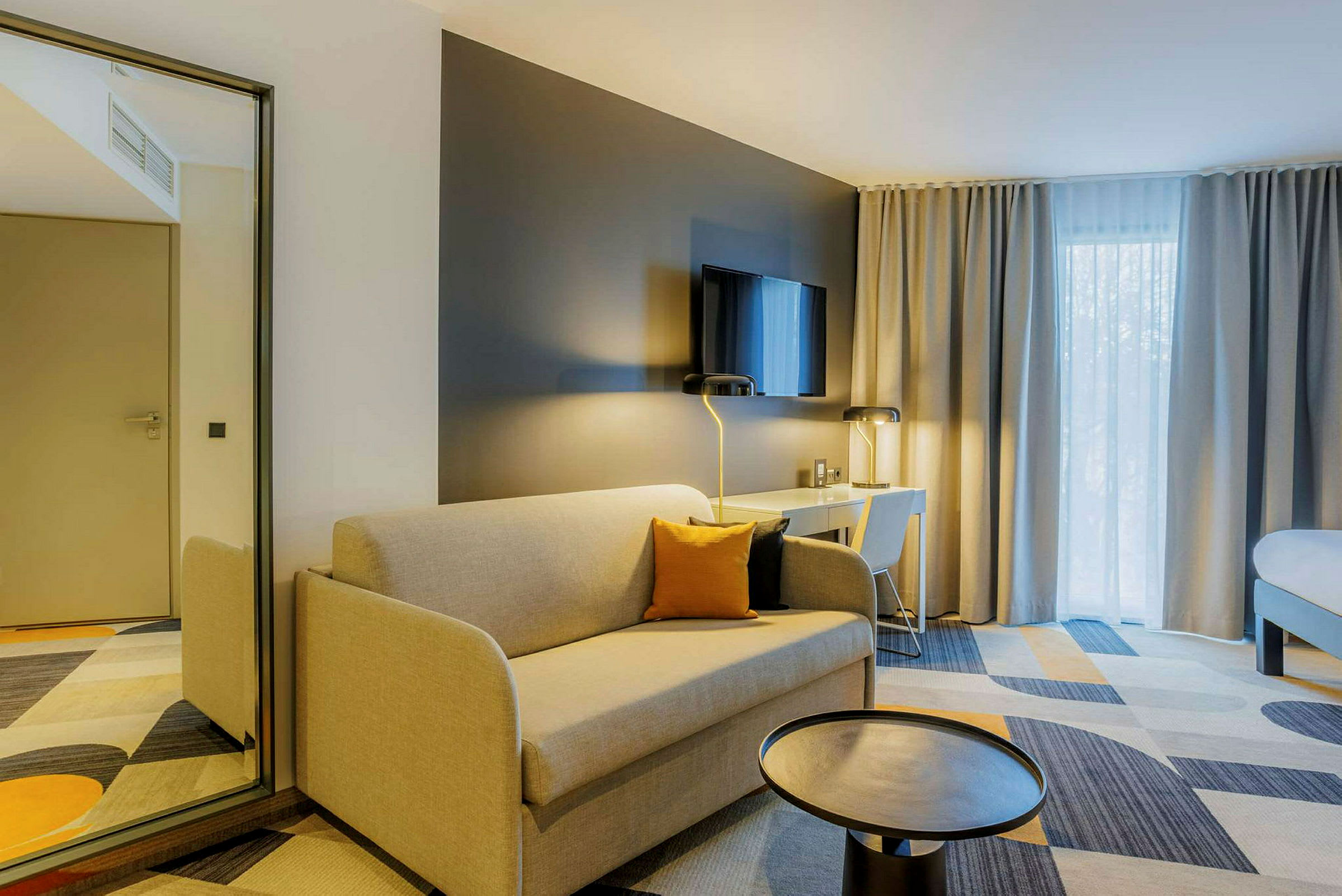 Moderne hotelværelse med beige sofa, sort bord, skrivebord med stol og tv på væggen. (AI-genereret tekst)