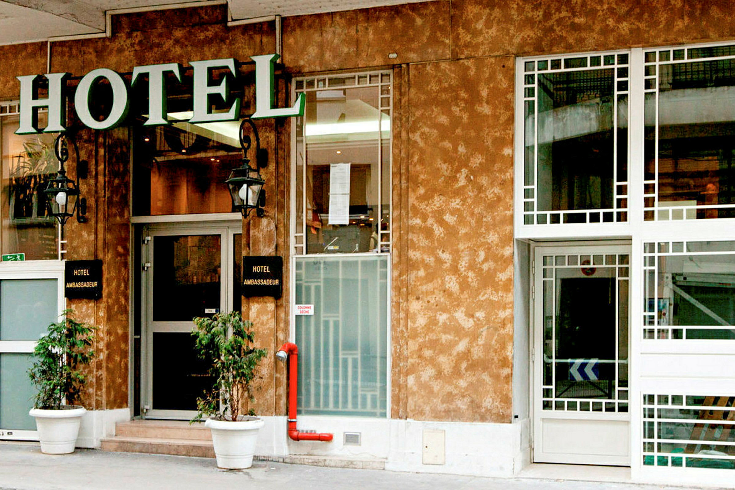 Forsiden af et hotel med et skilt, der siger 'Hotel Ambassadeur'. (AI-genereret tekst)