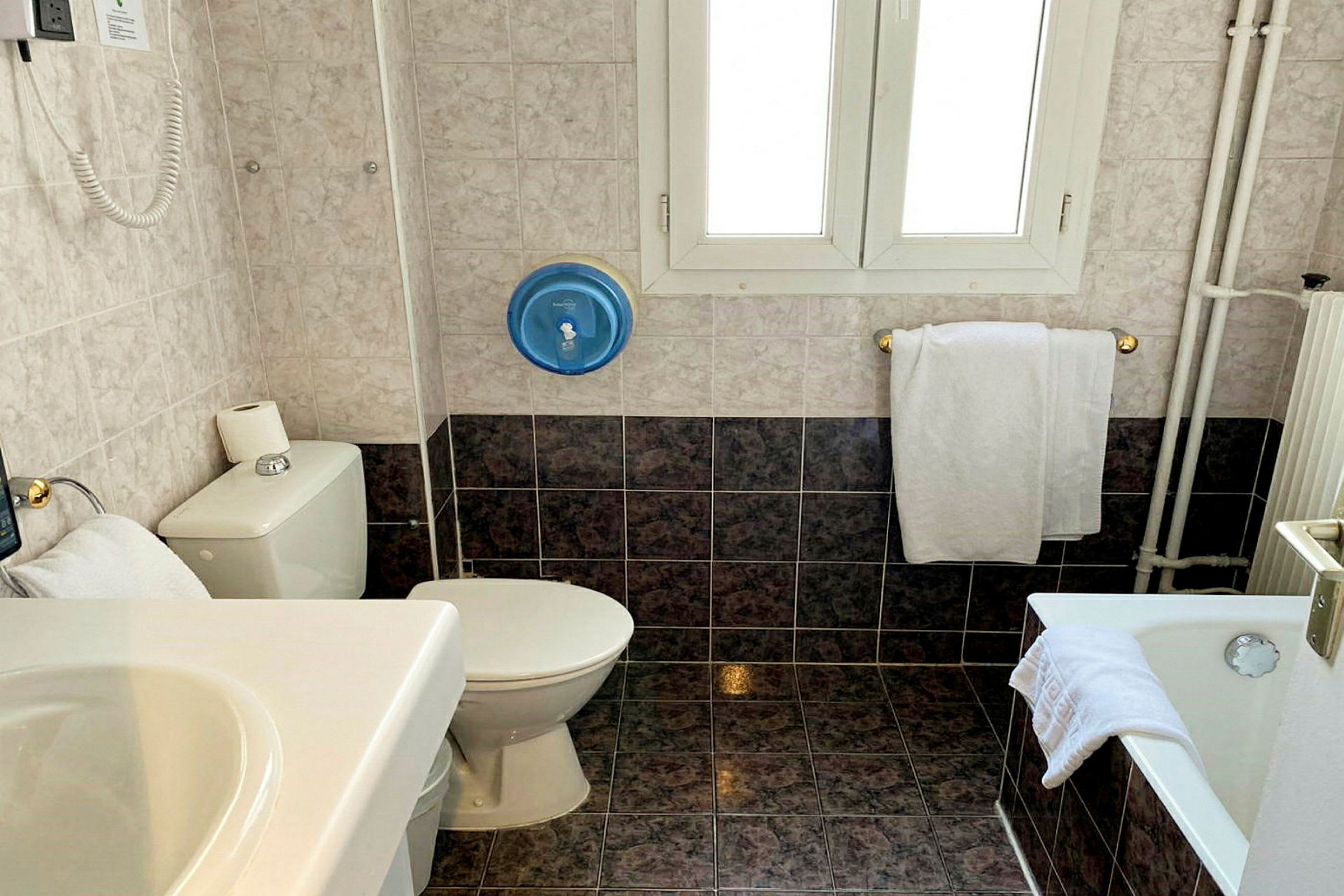 Et badeværelse med toilet, håndvask, badekar og håndklæder. (AI-genereret tekst)