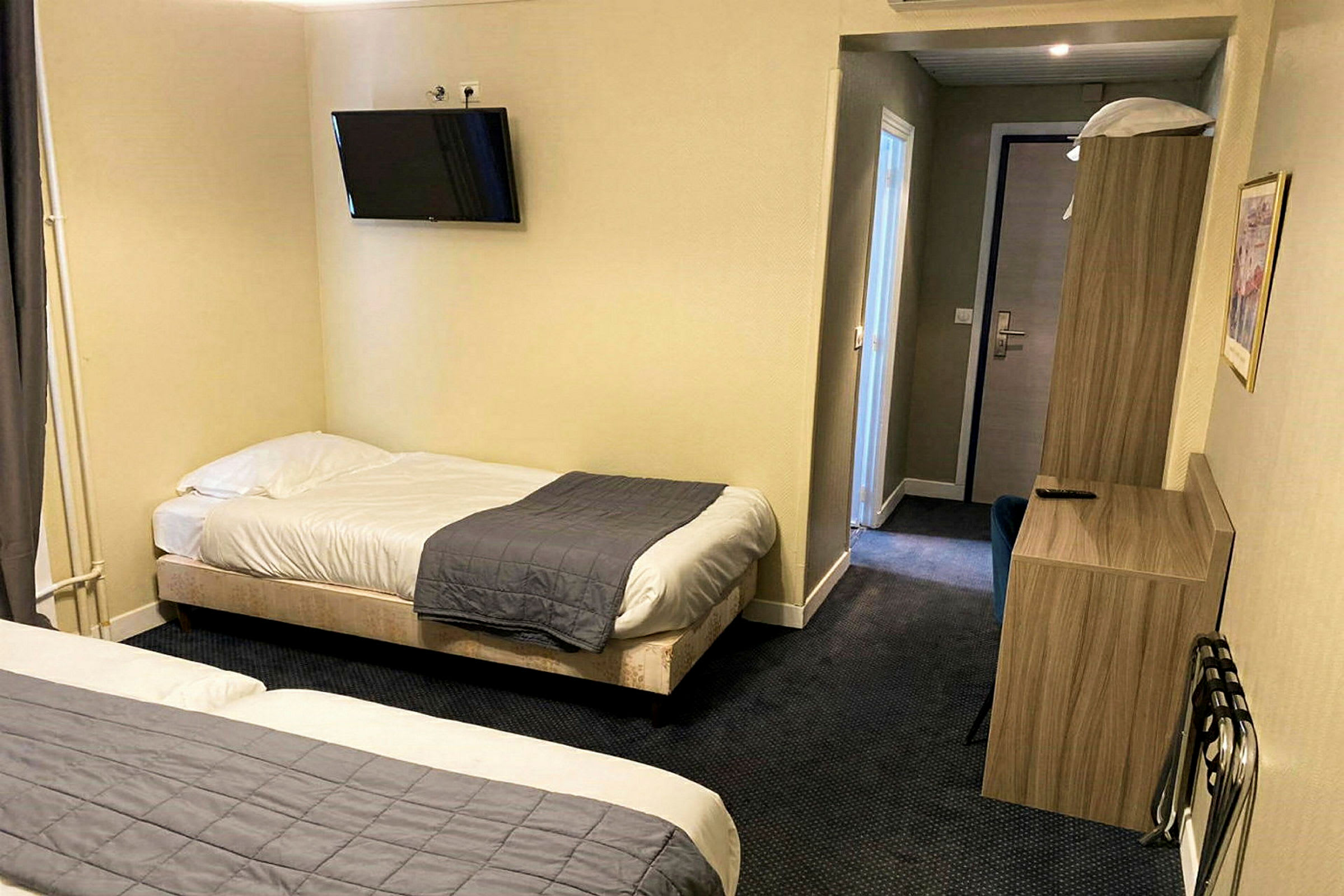 Et hotelværelse med to enkeltsenge, et vægmonteret TV og møbler. (AI-genereret tekst)