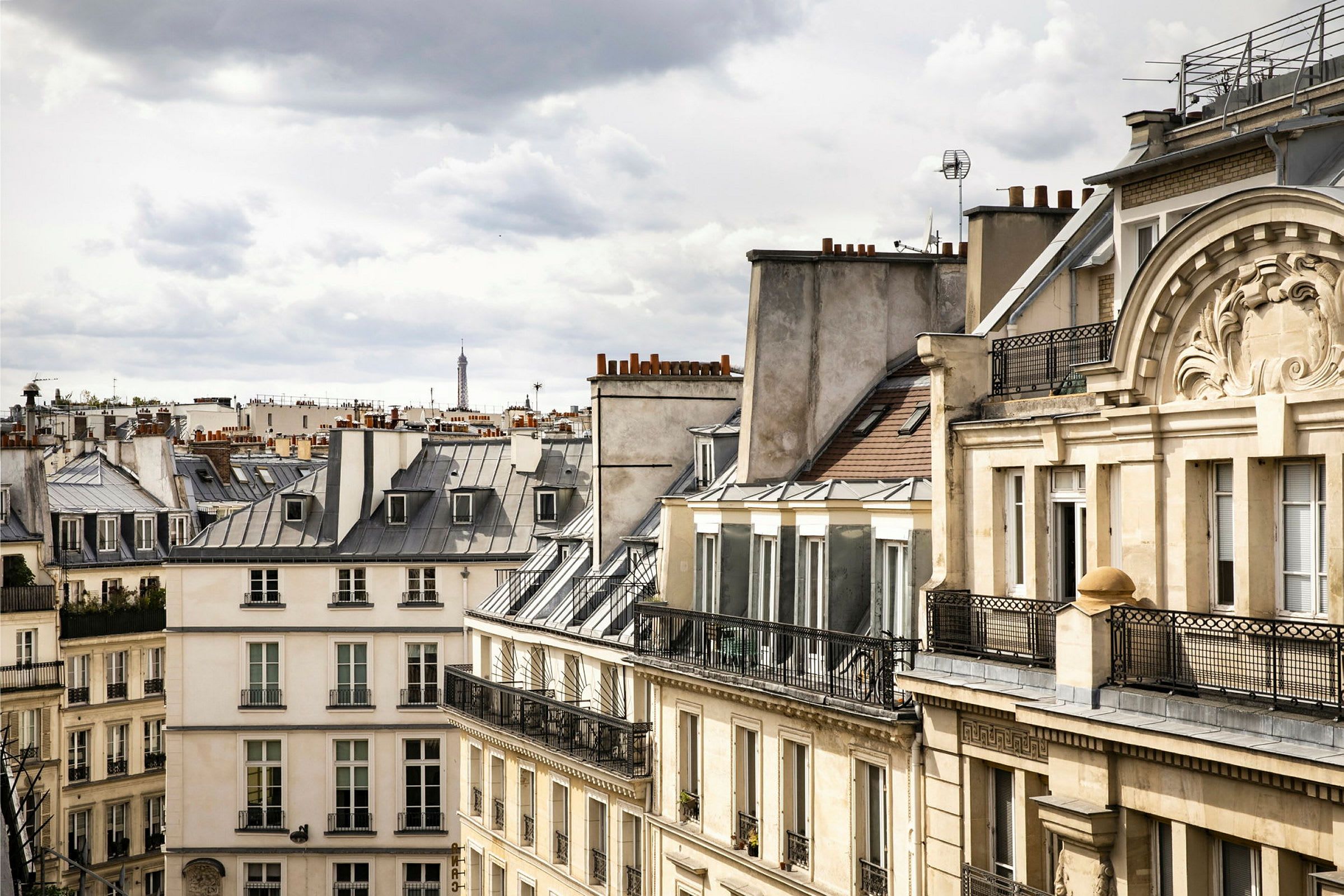 Billede af parisiske bygninger med typiske tage, med Eiffeltårnet synligt i baggrunden. (AI-genereret tekst)