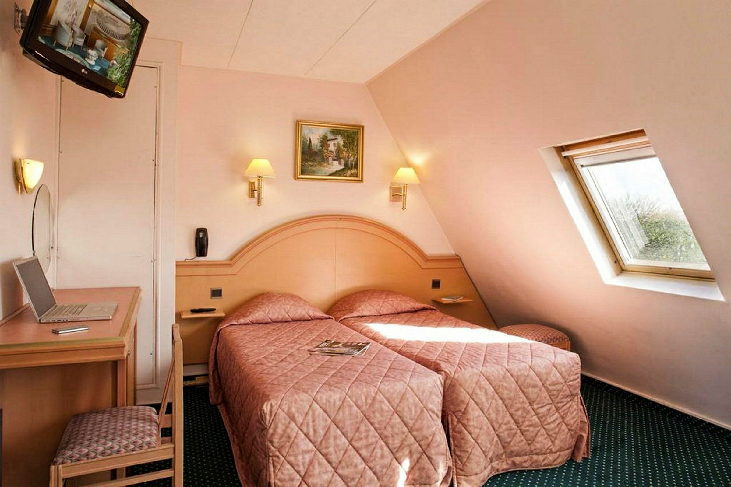 Et hotelværelse med to enkeltsenge med matchende sengetæpper. Et lille skrivebord og en stol står ved siden af, og et skråt stillet vindue lader naturligt lys komme ind. (AI-genereret tekst)