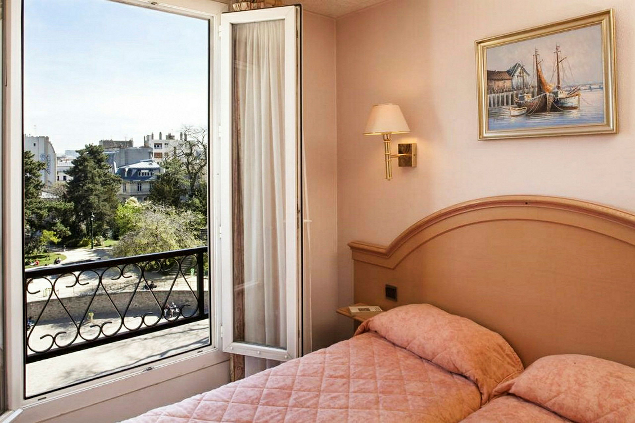 Et hotelværelse med en seng og en åben balkondør, der viser udsigt over en by og et grønt område. (AI-genereret tekst)