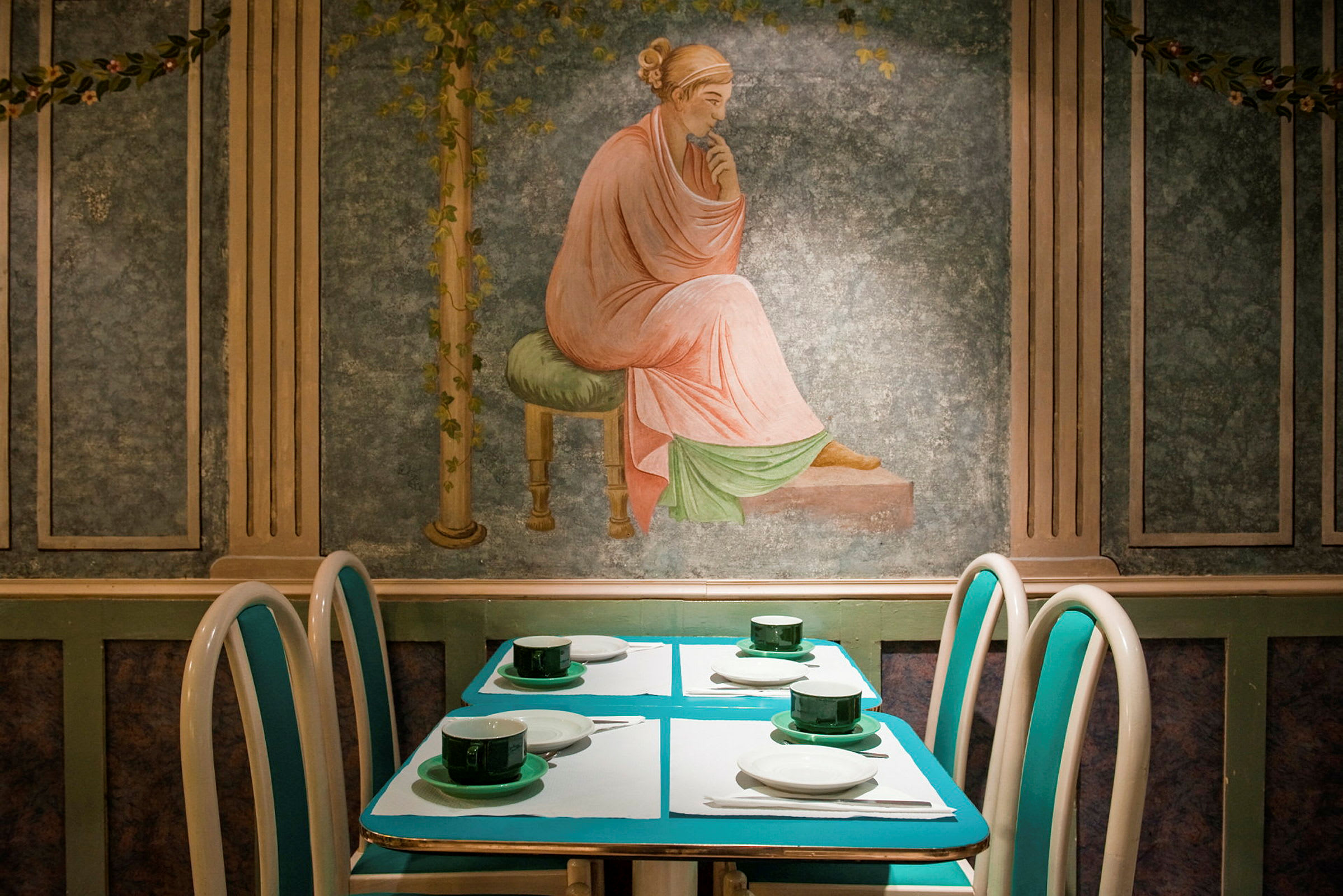 En opdækket restaurantbordopsætning med kunstnerisk vægmaleri i baggrunden. (AI-genereret tekst)