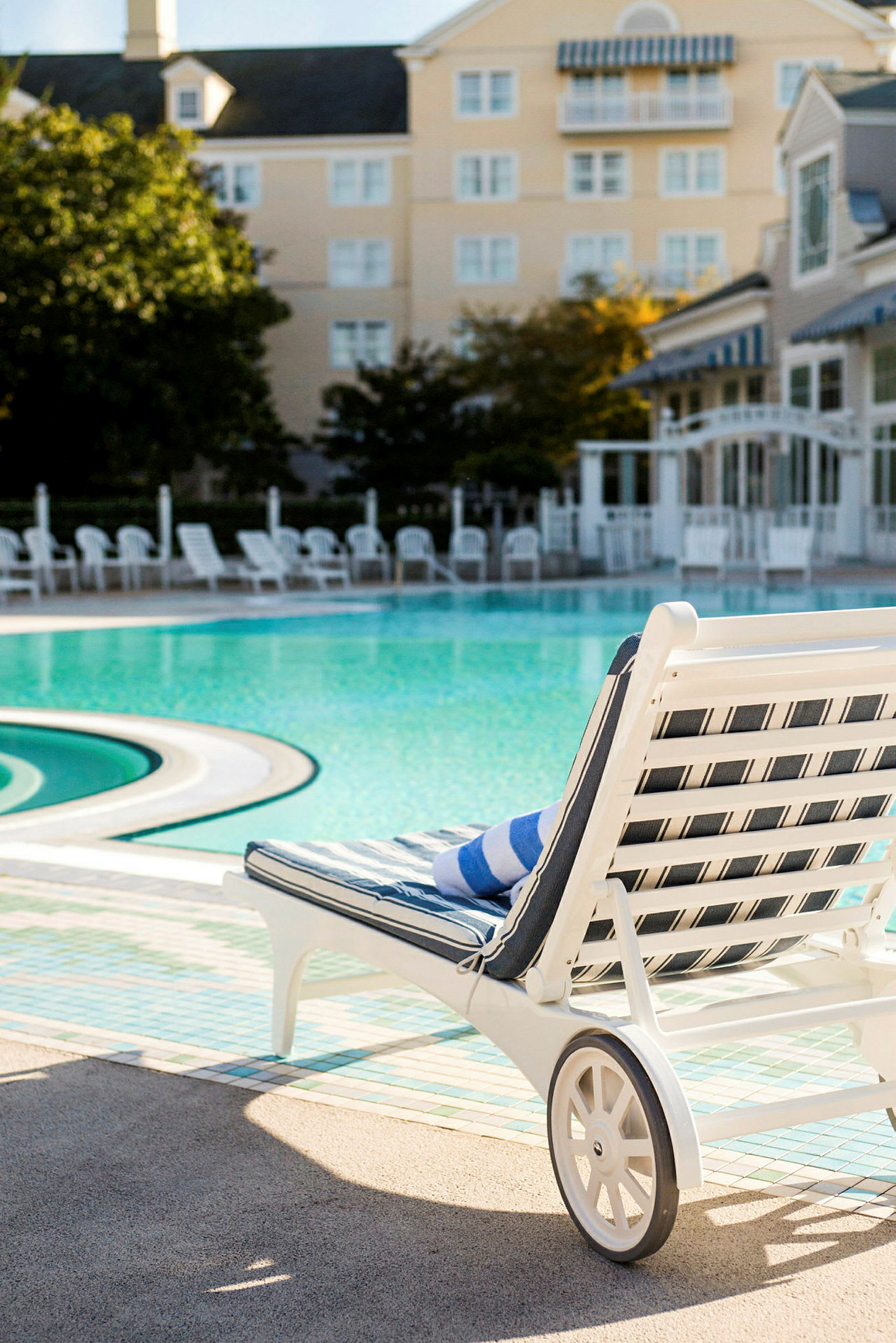 En liggestol med et blå- og hvidstribet håndklæde ved en udendørs swimmingpool. (AI-genereret tekst)