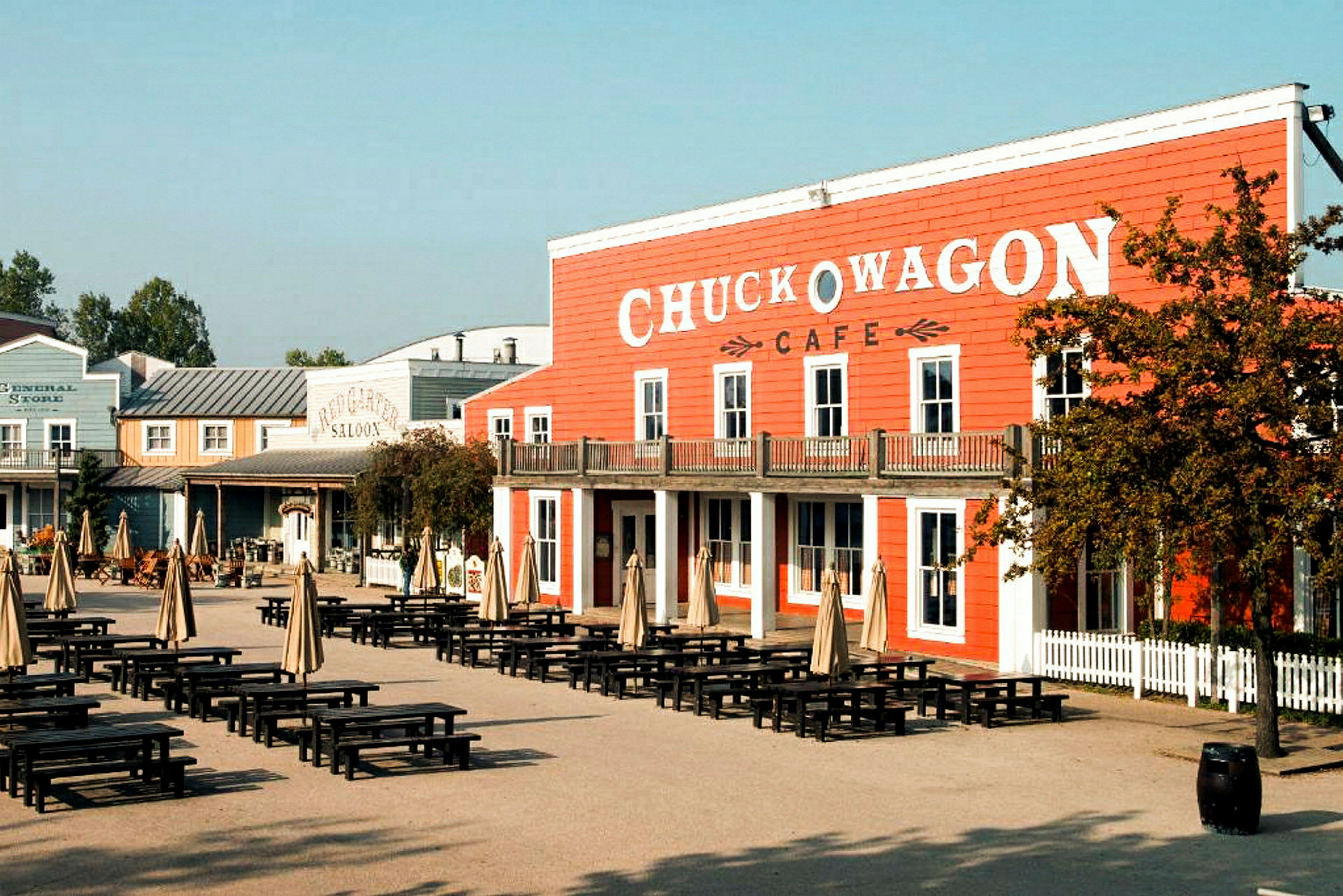 Et område med borde og parasoller foran en bygning med skiltet 'Chuck Wagon Cafe'. (AI-genereret tekst)