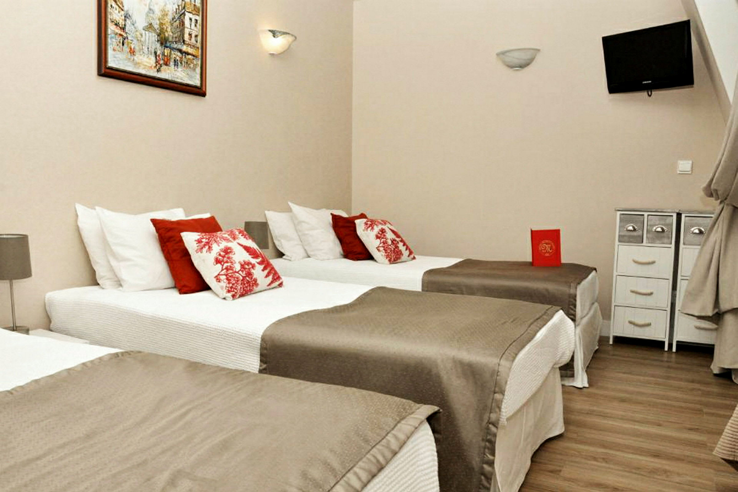Hotelværelse med tre enkeltsenge, dekoreret med røde og hvide puder. (AI-genereret tekst)