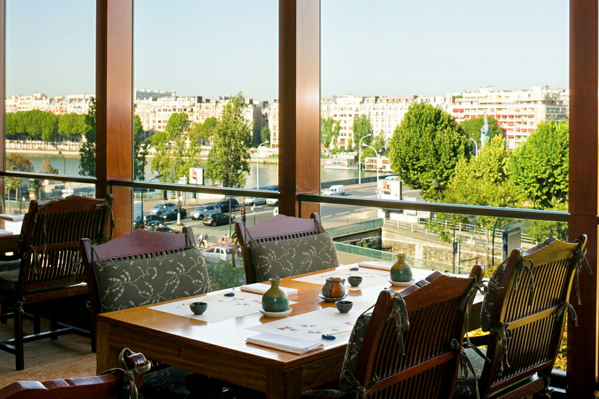 En restaurant med borde og stole tæt på et stort vindue med udsigt over byen og floden. (AI-genereret tekst)