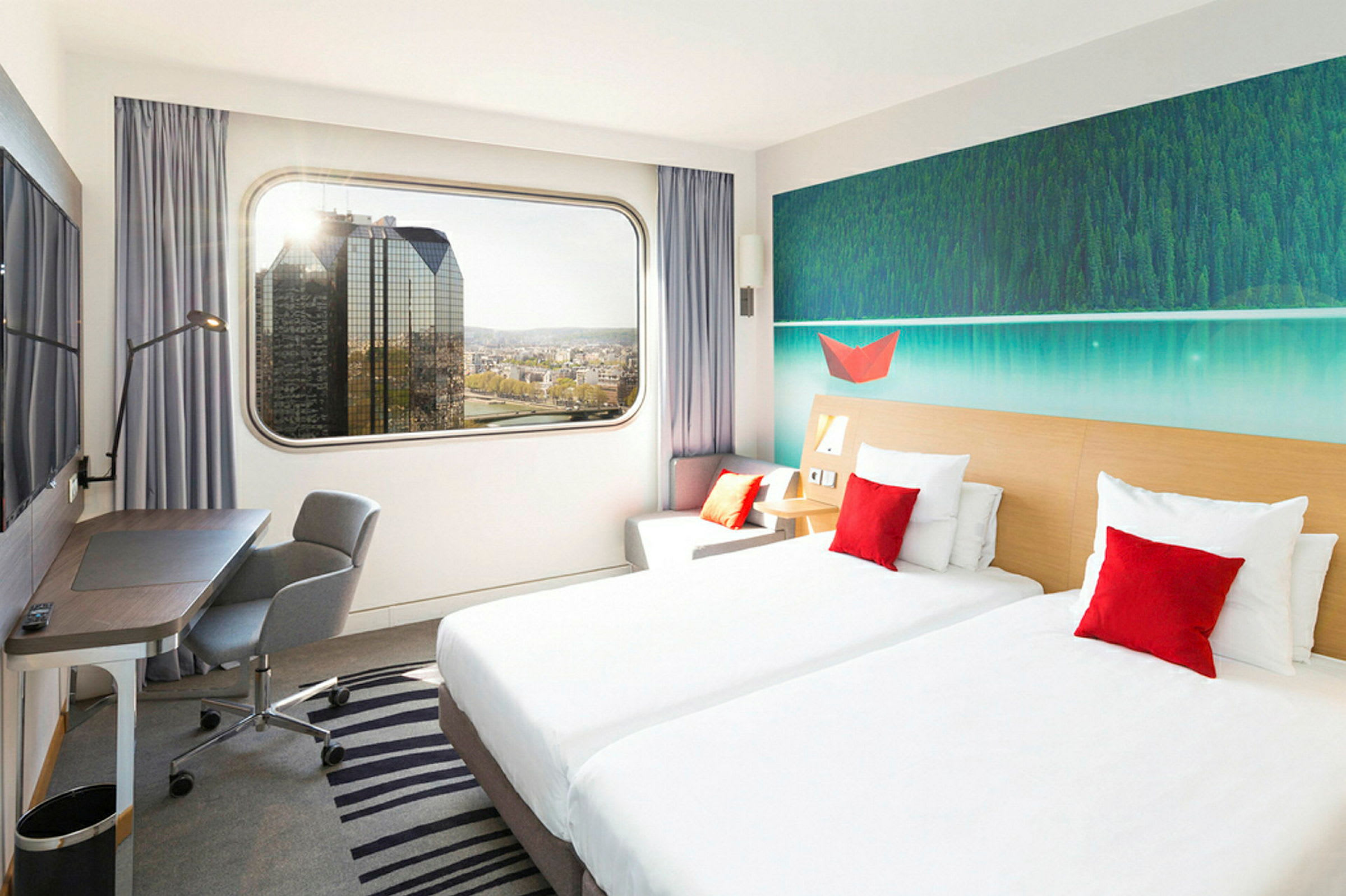Et hotelværelse med to enkeltsenge, en arbejdsplads og en stor vinduesudsigt over byens skyline. (AI-genereret tekst)