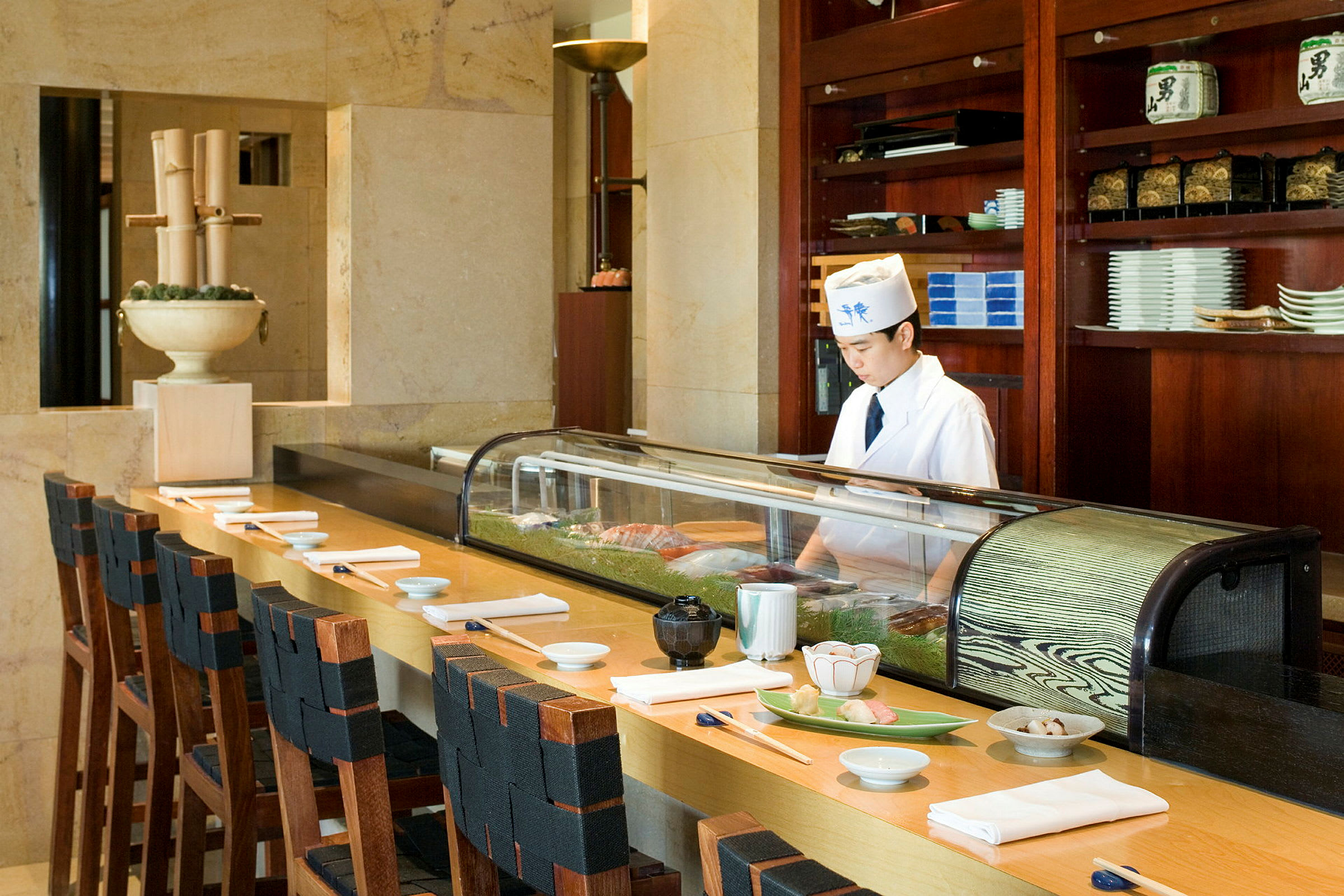En sushi-bar med stole ved en disk, klar med tallerkener og spisepinde. (AI-genereret tekst)