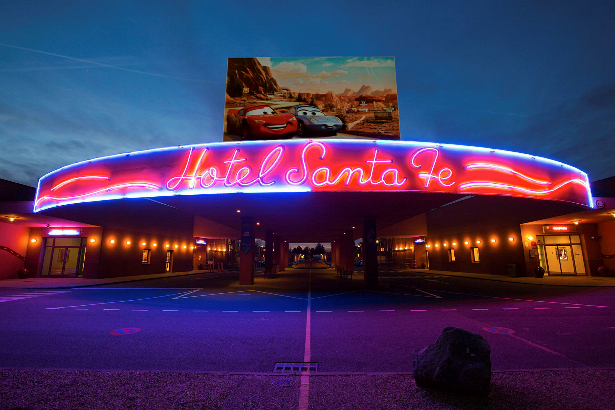 Neonskiltet over indgangen til Hotel Santa Fe med Disney/Pixar-biler på plakaten ovenover. (AI-genereret tekst)