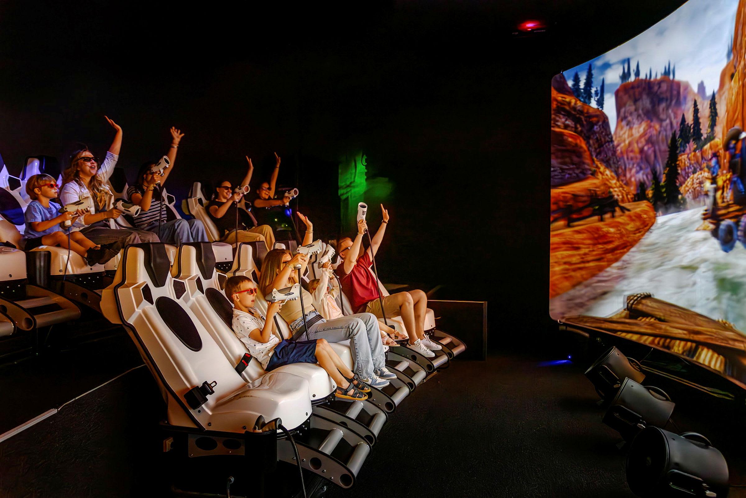 En gruppe personer sidder i en interaktiv simulator med en stor skærm, der viser en naturscene med bjerge og flod. (AI-genereret tekst)