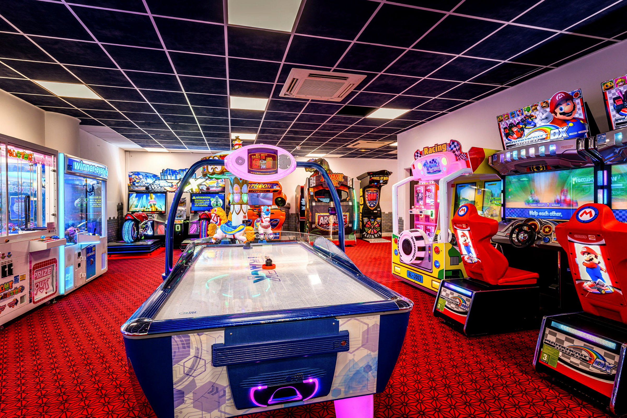 Et billede af et spillearkaderum med forskellige spillemaskiner og en airhockey-maskine i forgrunden. (AI-genereret tekst)